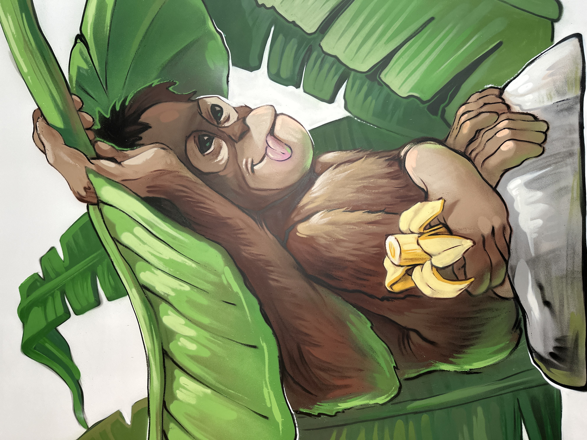 A cartoon image of an orangutan reclining among banana leaves and holding a bunch of bananas. The orangutan has brown fur and tan hands and face. Its tongue is sticking out, and its eyes are looking upward. The background consists of large, green banana leaves. The image appears to be a mural or decoration. There is no visual information in the image to indicate a location in Varna, Bulgaria.