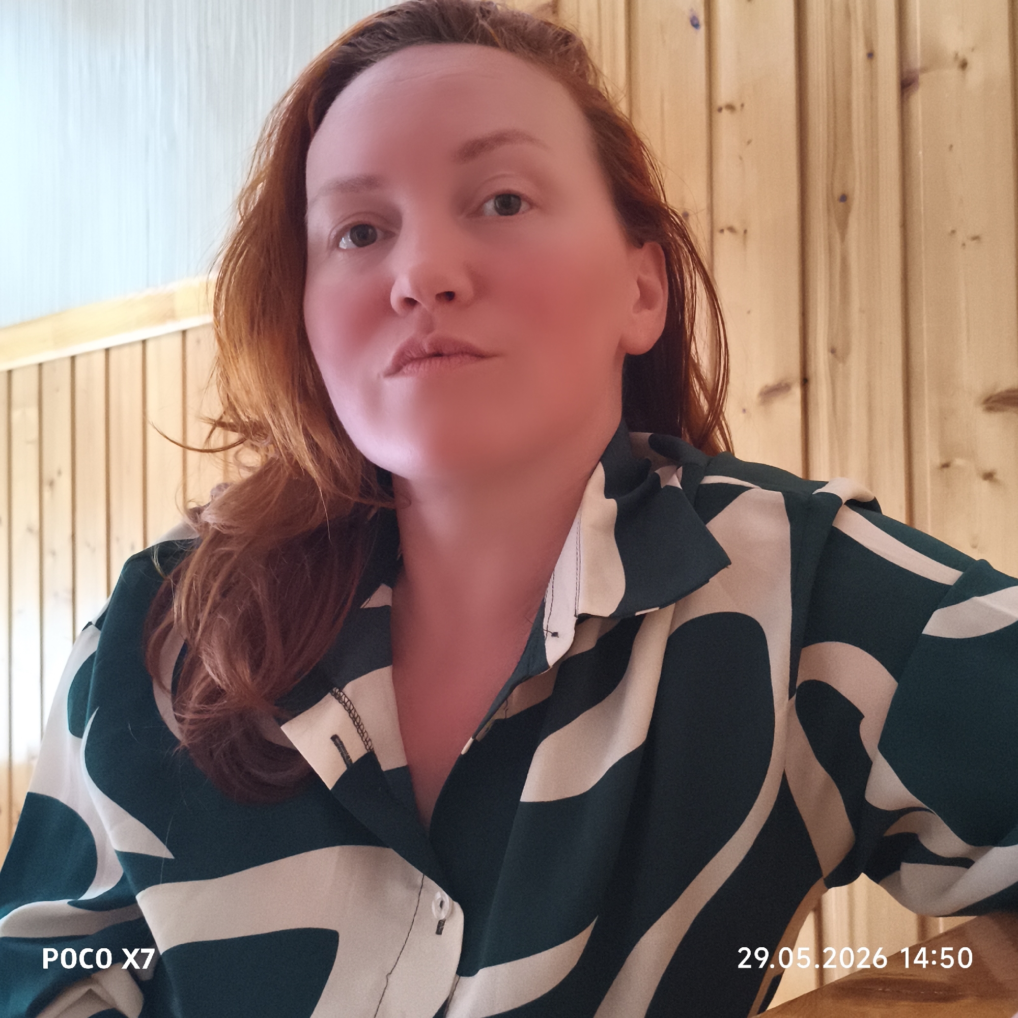 A woman with red hair is pictured in an indoor setting with wooden paneling in the background. She is wearing a green and white patterned shirt. The lower left corner of the image displays the text "POCO X7," while the lower right corner shows "29.05.2026 14:50." The location is listed as Unknown, Unknown.