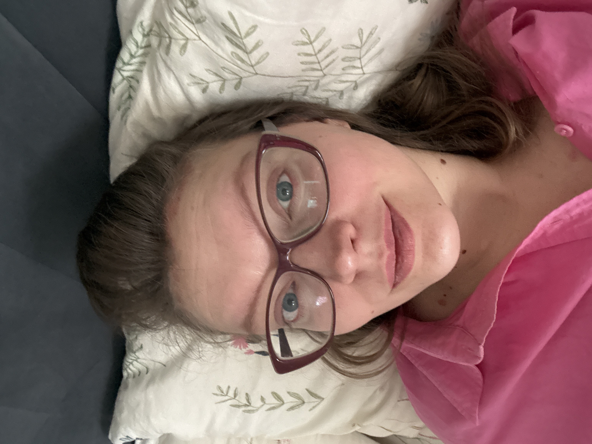 A woman is lying on a pillow, wearing glasses and a pink shirt. The pillow has a leaf pattern. She appears to be indoors. There is no information provided to indicate that this image was taken in Izhevsk, Russia.