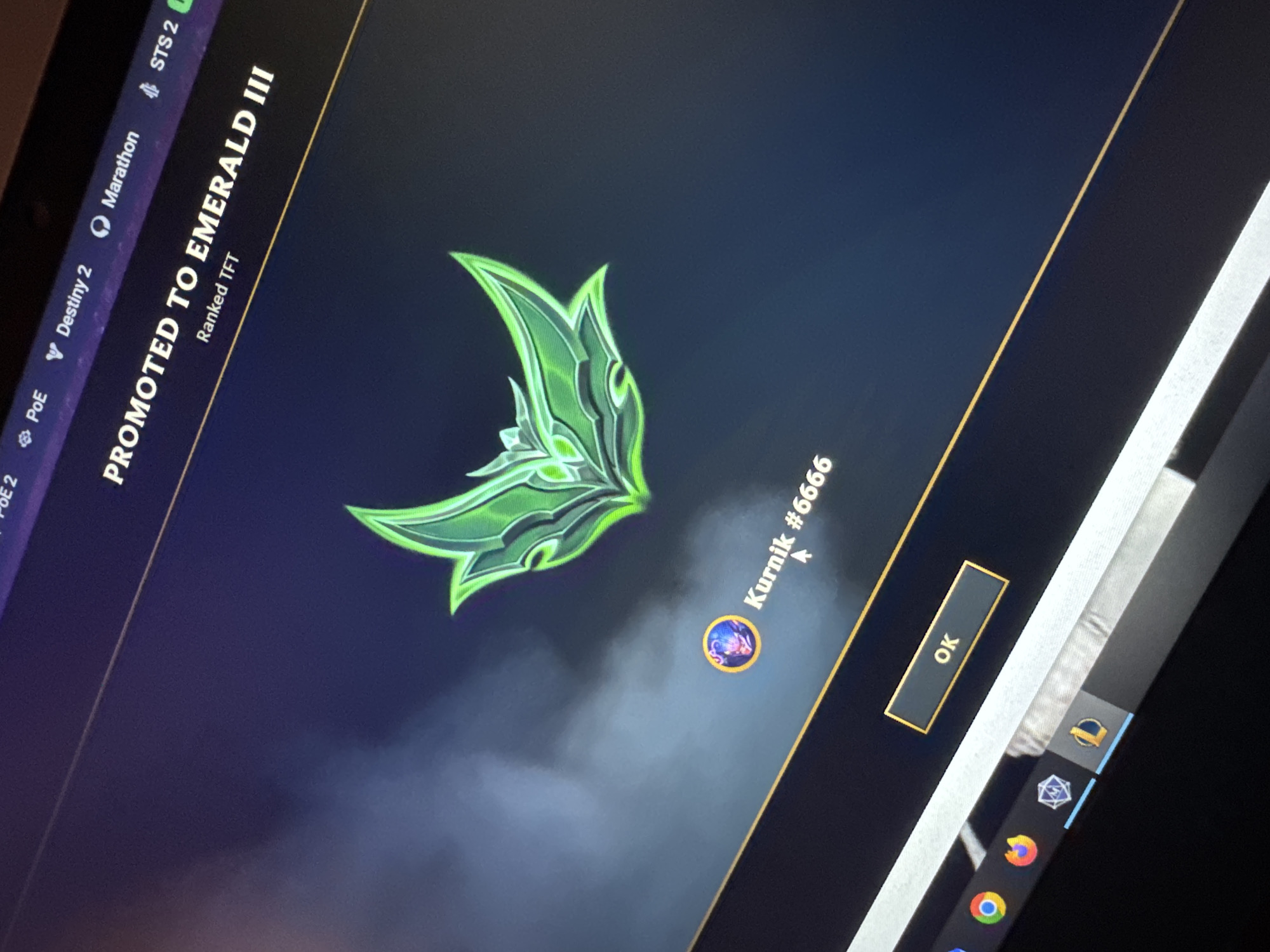 The image shows a computer screen displaying a promotion screen from the game Teamfight Tactics (TFT). The screen reads "PROMOTED TO EMERALD III" and includes a stylized green emblem associated with the Emerald rank. Below the emblem is the username "Kurnik #6666". An "OK" button is visible for confirmation. Icons for other programs, including "PoE 2", "Destiny 2", "Marathon", and "STS 2" are displayed at the top of the screen. The taskbar at the bottom shows icons for programs such as Google Chrome and the League of Legends client. The city of Dolna Oryahovitsa, Bulgaria, is not depicted in the image and is therefore irrelevant.