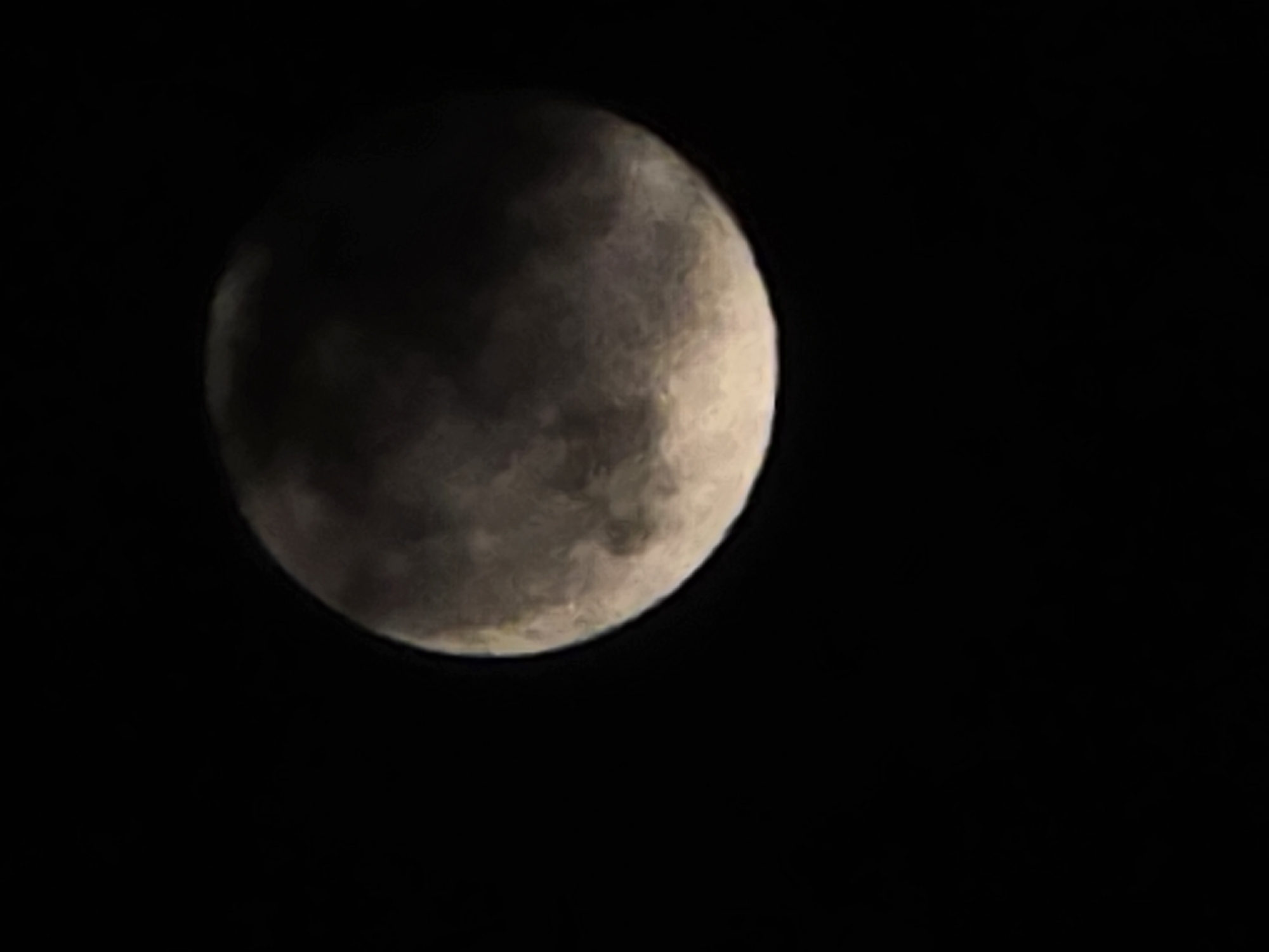 The image shows the moon, partially obscured by clouds. It appears to be a crescent shape with the right side illuminated and the left side in shadow or hidden behind clouds. The background is black, indicating a night sky. The location is Unknown, Unknown.
