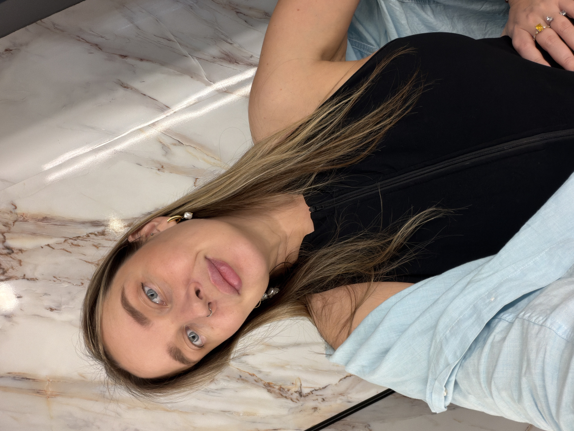 A woman lies on a marble surface. She wears a black top, light blue shirt, and several rings on her right hand. She has a nose ring and earrings. The floor appears to be made of marble. The location cannot be determined as Moscow, Russia.