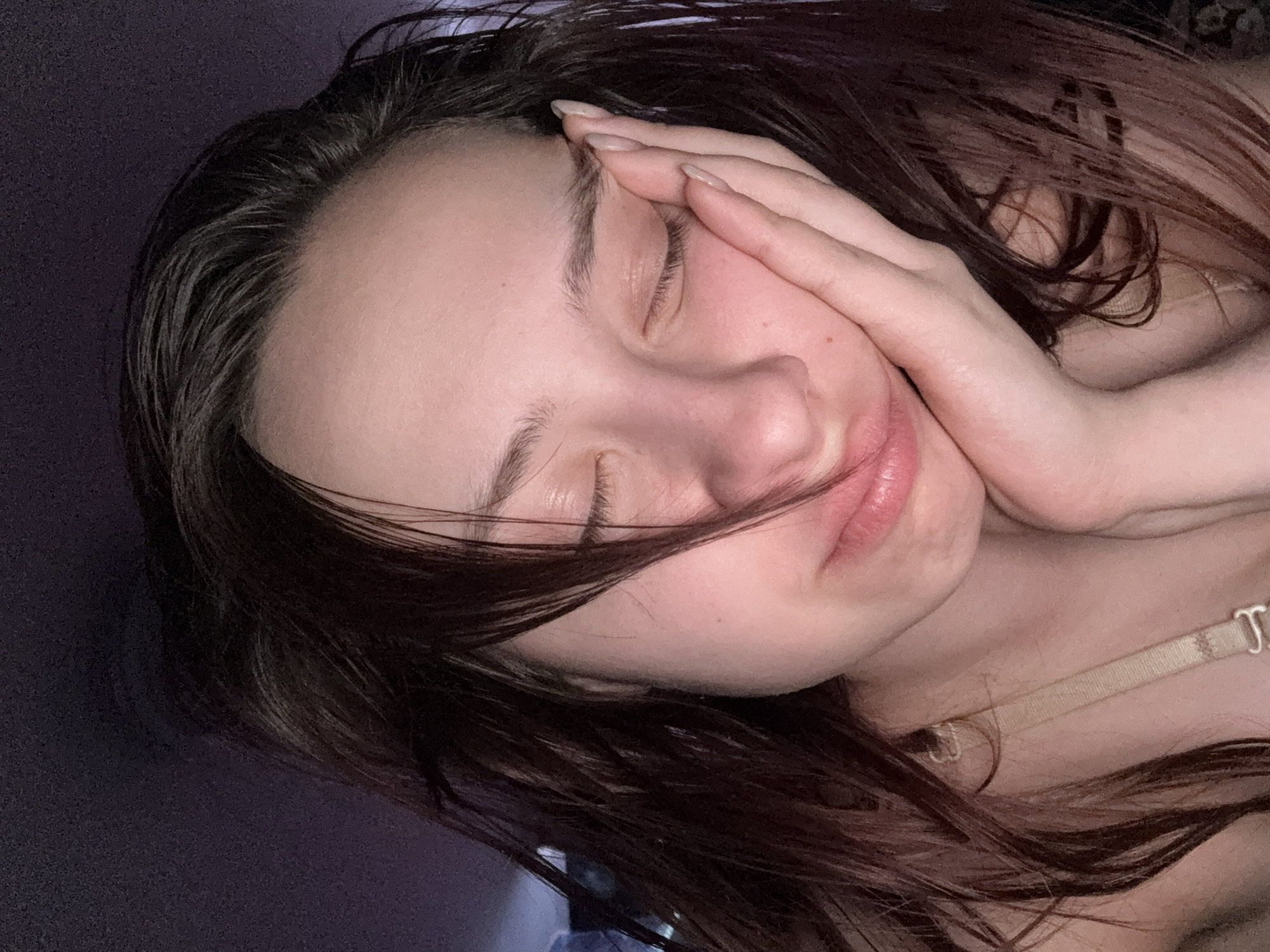 A woman with long, dark hair is lying down with her eyes closed and her hand resting on her face. The location is Прикамский, Russia. There are no other people, subjects, objects or actions visible in the image. The environment appears to be indoors, possibly a bedroom.
