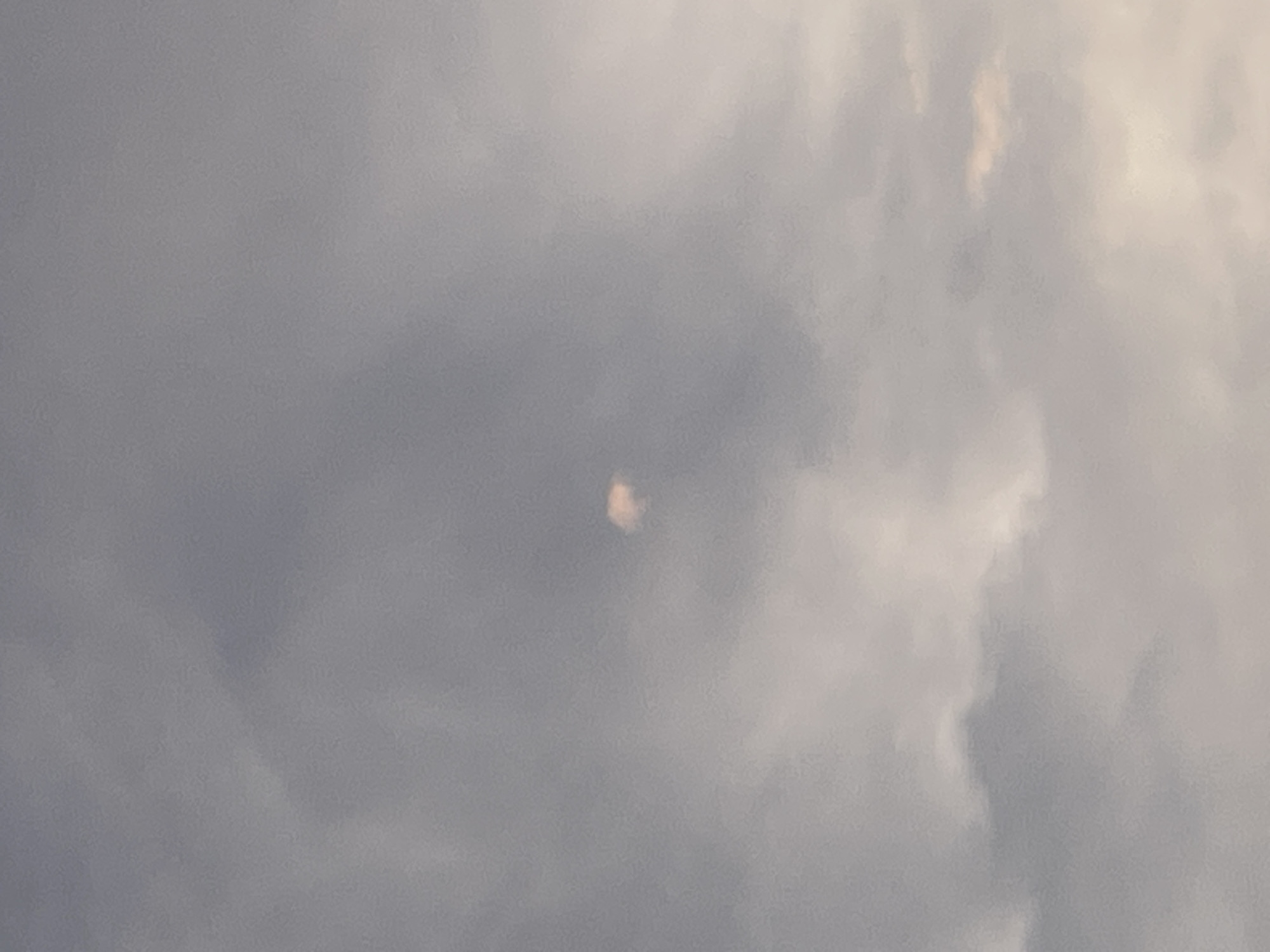 A small, bright, object, possibly a cloud illuminated by sunlight, is visible in the center of a cloudy sky. The sky is predominantly gray with some lighter patches. The image is taken from a ground-level perspective, looking upwards. There are no visible people, buildings, or other objects in the frame. The specific location in Gerstheim, France, cannot be determined from the image alone.