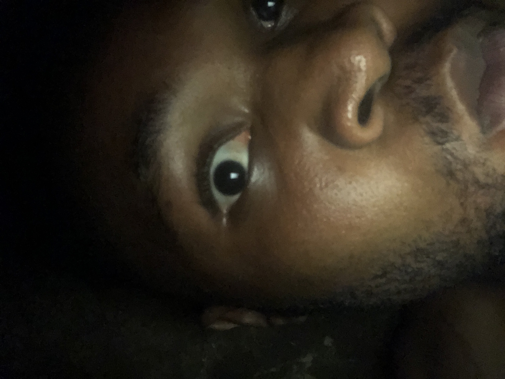 A close-up, rotated image shows a person's face. The person has dark skin, dark eyes, and short dark facial hair. The person's mouth is slightly open. The setting or city is not discernible.