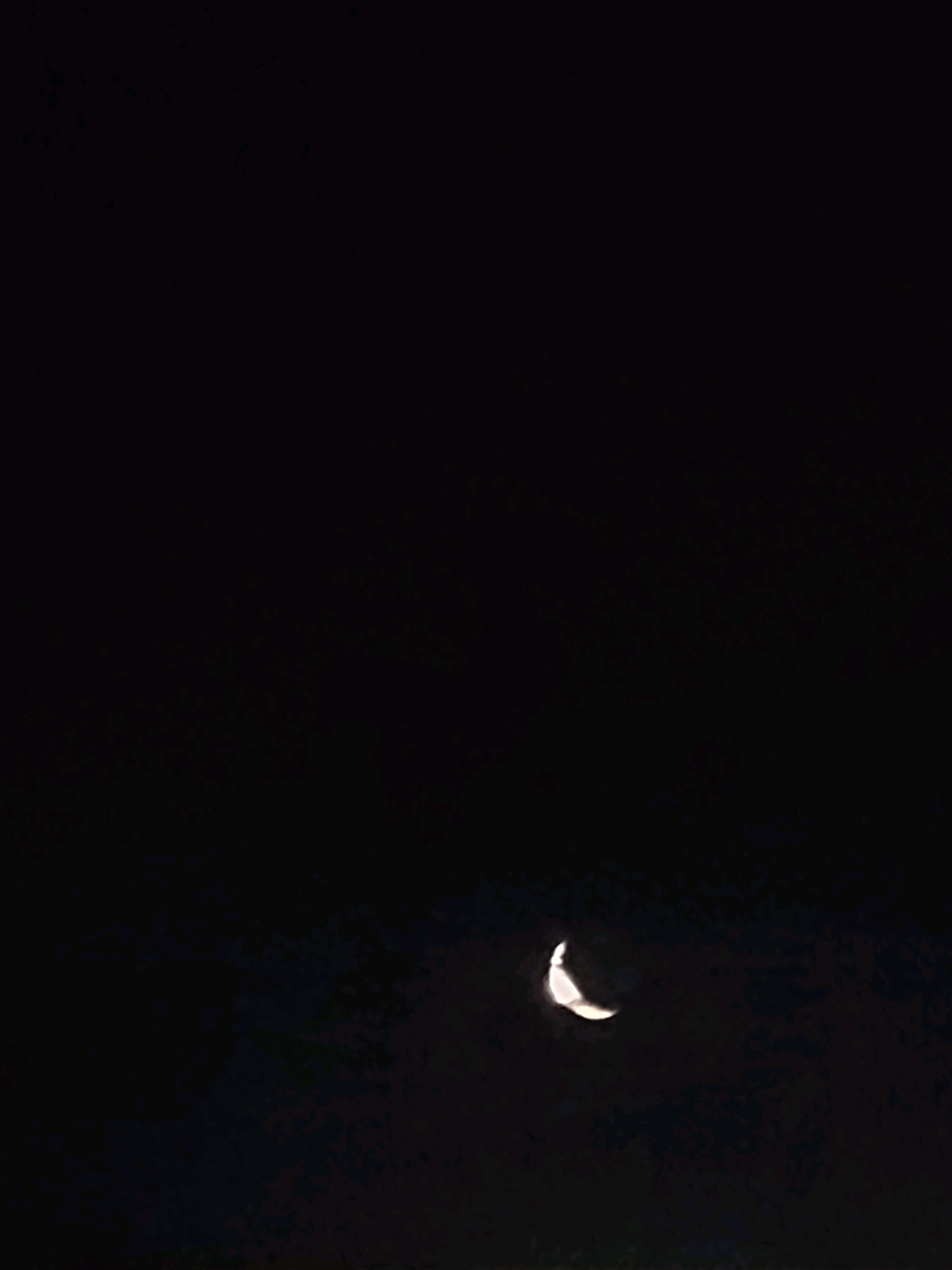 A crescent moon is visible in a dark night sky. The moon is partially illuminated and positioned in the lower right quadrant of the image. The background is uniformly dark, suggesting a nighttime environment with minimal light pollution. There are no visible structures or geographical features that would specifically place this image in Ozolnieki, Latvia.