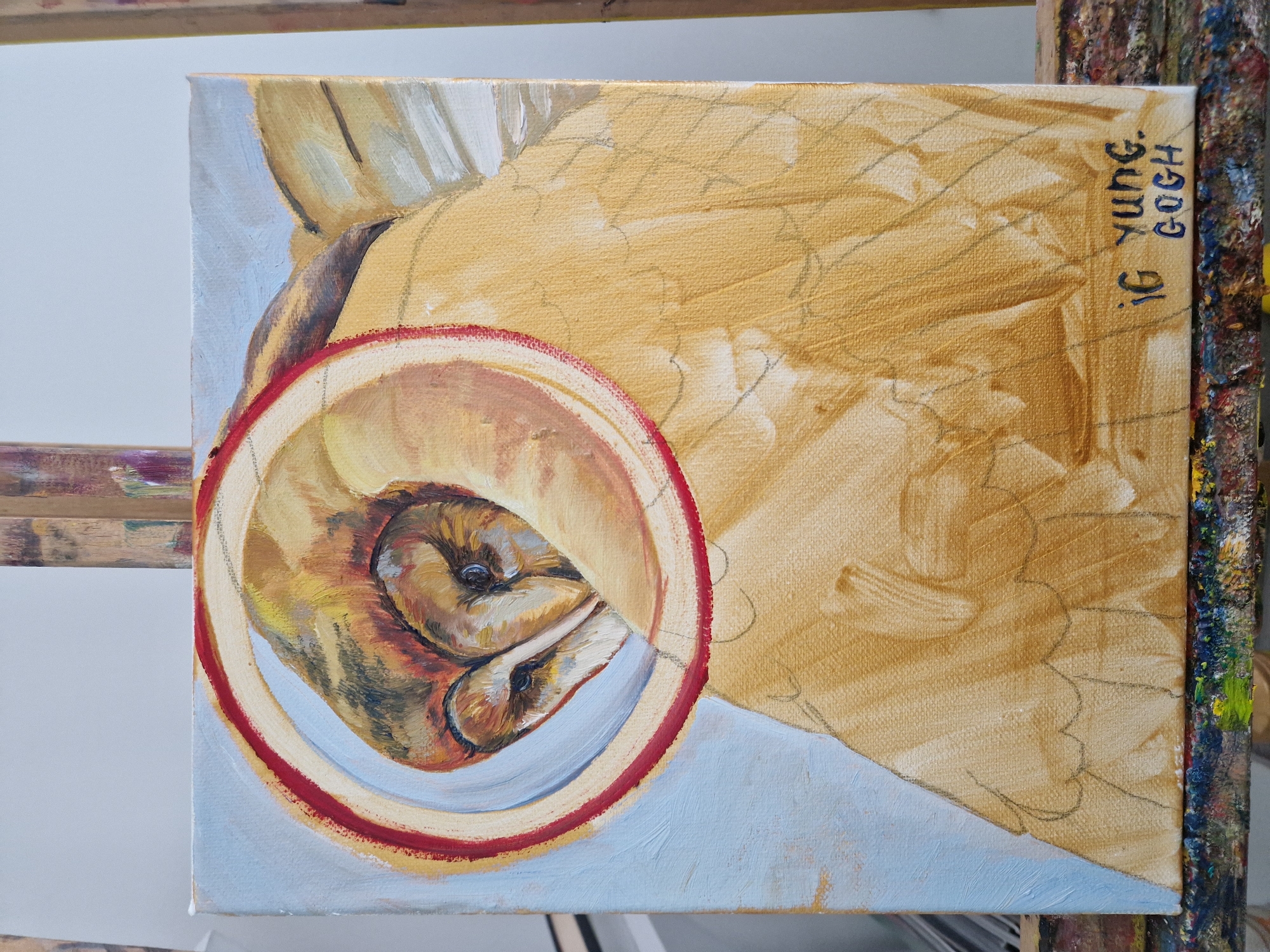 The image shows an unfinished oil painting of an owl on a canvas, resting on a paint-splattered easel. The owl's face is within a red and tan circular frame, with the body extending beyond the circle. The background is a light blue color, and the rest of the canvas is a tan color. Text, "IG YUNG. GOGH" is written in blue on the upper-right corner of the canvas. The painting appears to be a work in progress, with sketched outlines visible and varying levels of detail in the rendering of the owl. The city location is Unknown, Unknown.