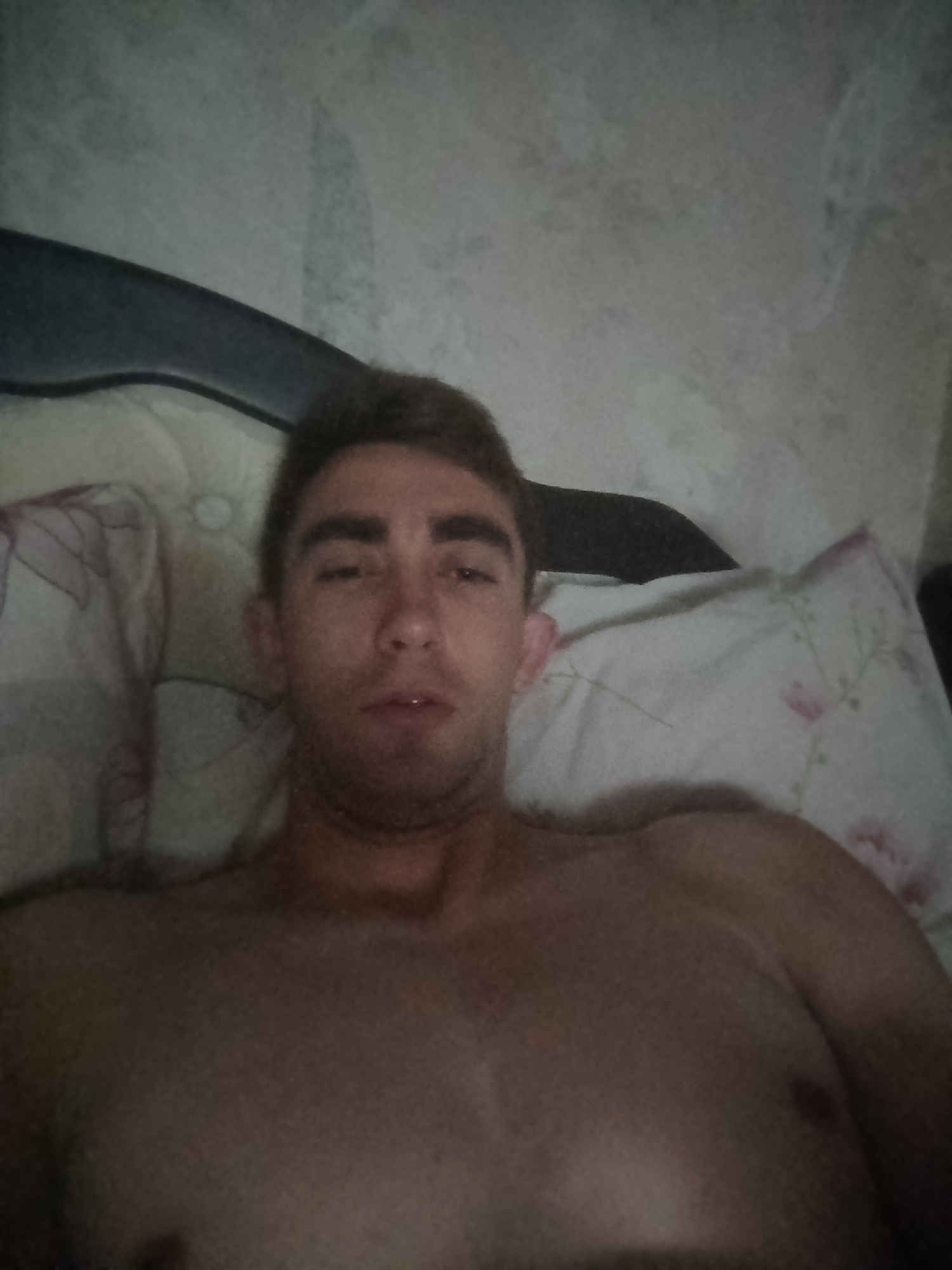 A man with short brown hair and brown eyes is lying down in bed. He is shirtless and his head is resting on a pillow. The background appears to be a wall with a textured pattern. The image does not provide any specific details about the city of Fastiv, Ukraine.