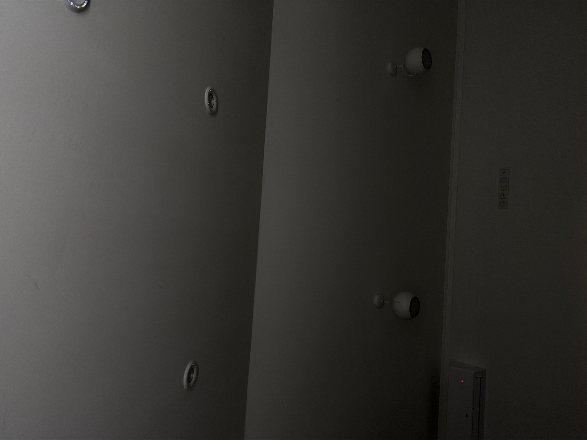 A ceiling with recessed lights and pendant lights is visible in the image. On the wall below, an air conditioning unit with a red indicator light is mounted, alongside a power strip with multiple outlets. The environment appears to be indoors.