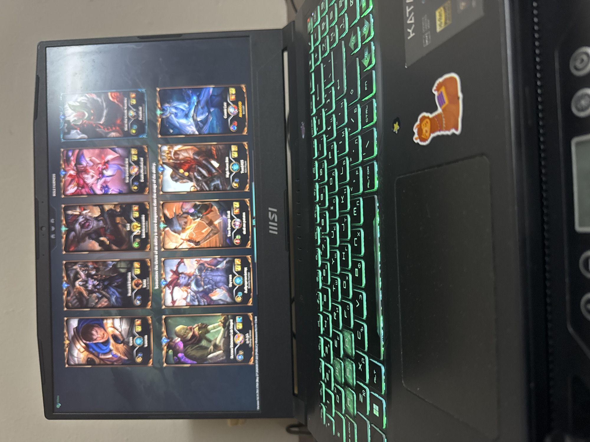 The image shows a laptop displaying a card game. The laptop keyboard is backlit in green. A sticker of a llama is on the laptop to the right of the trackpad. The laptop is a MSI brand. The card game shown on the laptop is Legends of Runeterra. The environment appears to be indoors. The image does not contain any information regarding the city of Sofia, Bulgaria.