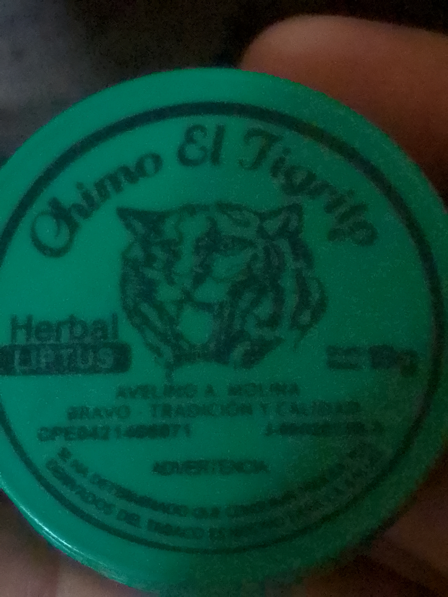 The image shows a green circular tin with the words "Chimo El Tigrito" printed on the top in dark lettering. Below the text is a drawing of a tiger's face. Underneath the tiger's face are the words "Herbal LIFTUS" in dark, block lettering. Further down, the tin reads "AVELINO A MOLINA BRAVO - TRADICION Y CALIDAD OPE04211406871 J-00030325". At the bottom of the tin is the word "ADVERTENCIA" and additional text that appears to be about the dangers associated with tobacco use. The location "Juan Griego, Venezuela" is not explicitly written on the tin.