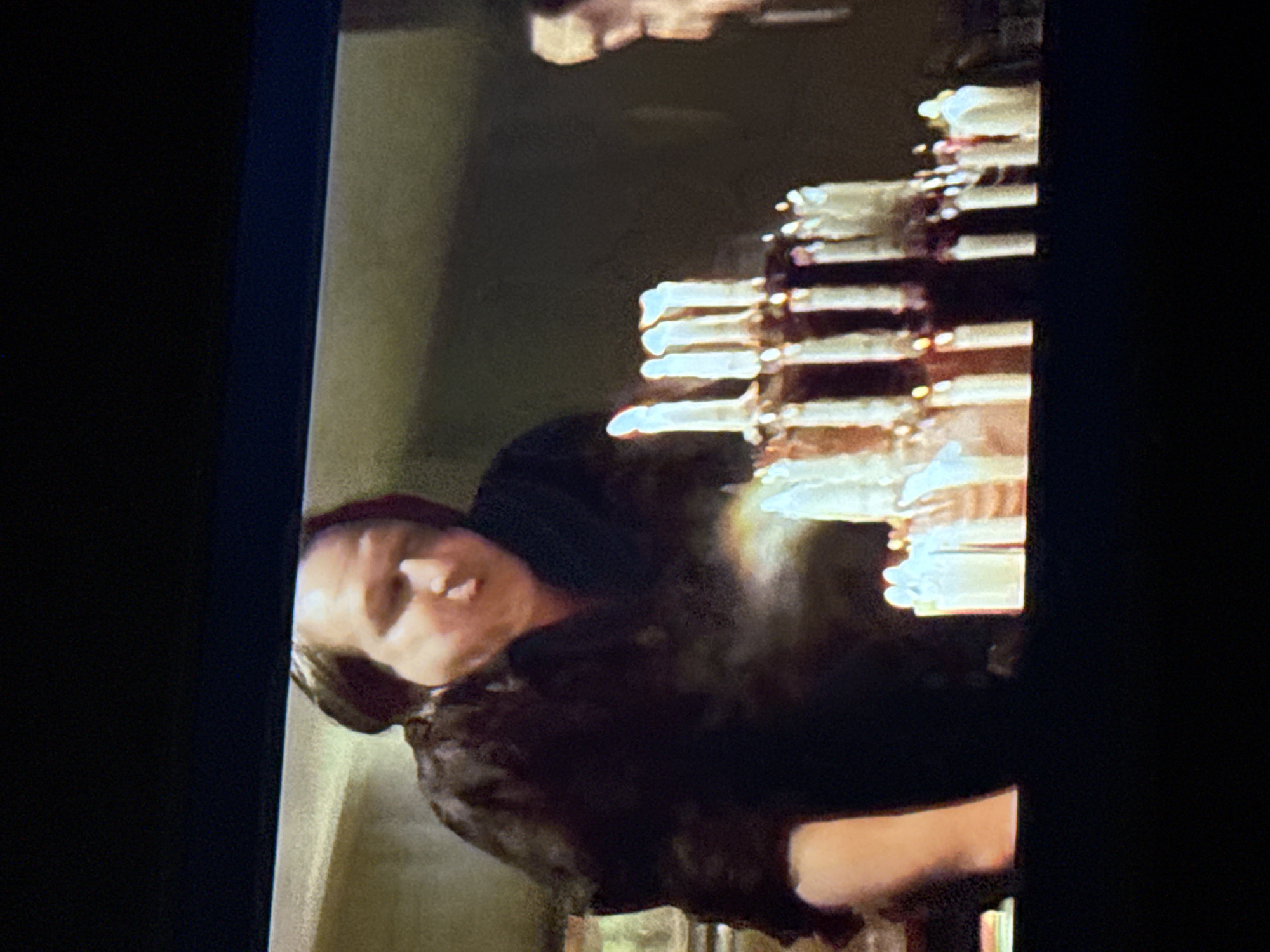 The image shows a person wearing dark clothing and headwear next to a table with multiple small, cylindrical objects. The objects have reflective tops. The location is not evident from the image.