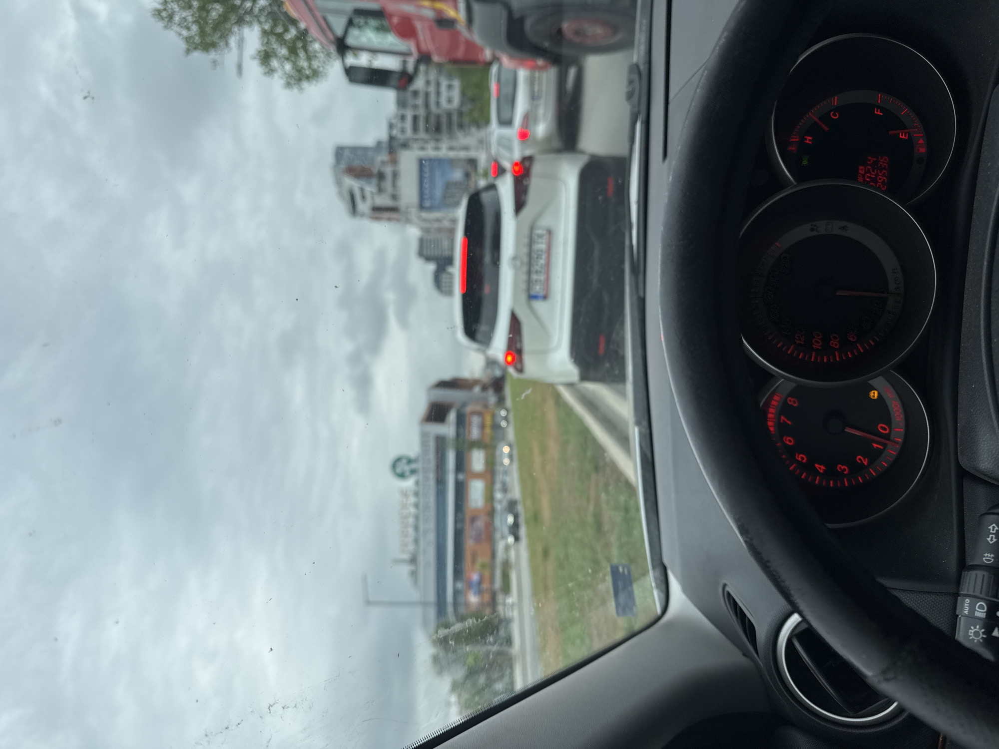 The image, taken from inside a car, shows heavy traffic on a city street. In the foreground, the car's dashboard is visible, including the speedometer and fuel gauge. The needle on the fuel gauge is pointing to "E", indicating that the fuel tank is empty. The odometer reads 29536. Beyond the windshield, a line of cars stretches into the distance. A white vehicle with Bulgarian license plates is directly in front. Buildings line the street, including one with a large "Starbucks" logo. The sky is overcast. This location is the city of Sofia, Bulgaria.