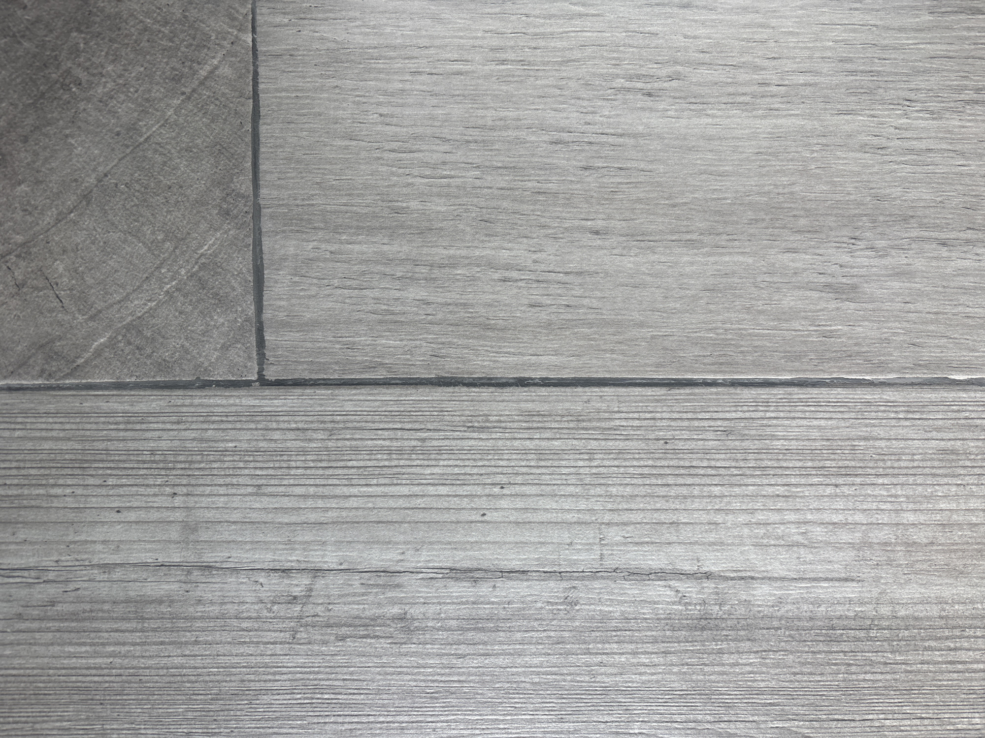The image shows a close-up view of gray-toned, rectangular flooring tiles. The surface appears to be textured, with a pattern resembling wood grain on two of the tiles and a diagonally-oriented, textured pattern on the third. The tiles are laid horizontally with dark-colored grout lines separating them. The bottom two tiles have a pattern of tight, horizontal lines. The image appears to be taken indoors under neutral lighting. The location in Buenavista, Mexico is undetermined from the image.