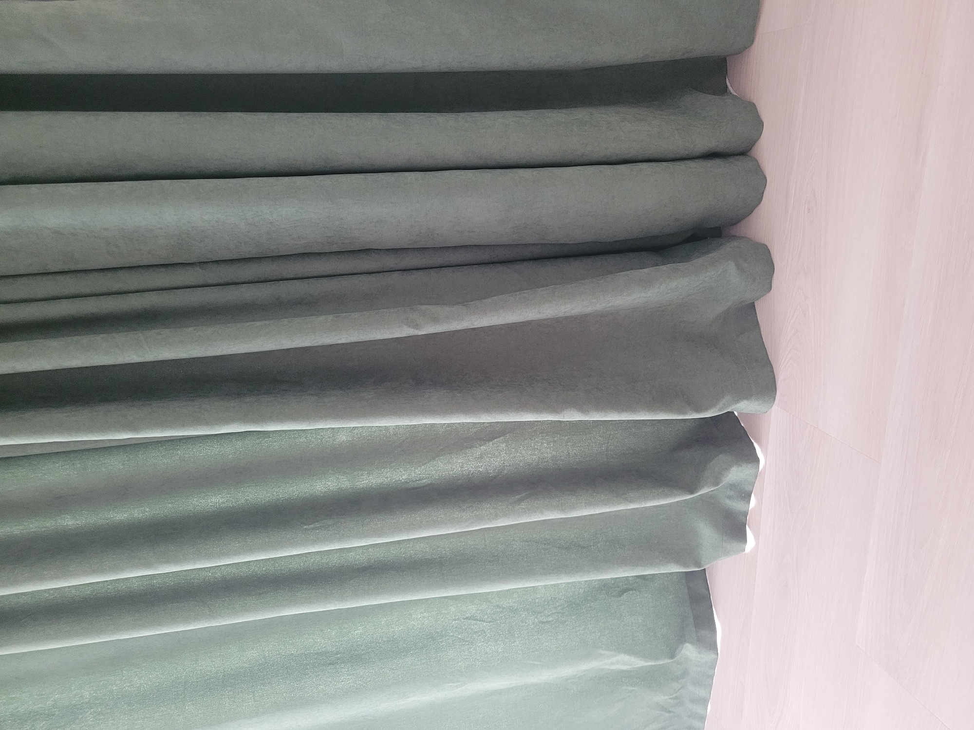 This media file shows a close-up, abstract view of a folded, dark green fabric, possibly a curtain or drape. The fabric has a soft texture and is arranged in deep, horizontal pleats. Sunlight or artificial light creates shadows and highlights within the folds, adding depth and dimension. To the right of the fabric, a light-colored, subtly textured surface, likely a wall or paneling, is visible. The overall impression is one of quiet stillness and texture. There is no discernible text, people, or activity. The setting is likely indoors, given the presence of the fabric and wall. The abstract nature of the shot makes it difficult to determine a specific time of day or weather conditions. The location context provided, Kyiv, Ukraine, does not offer direct visual cues within the image itself.