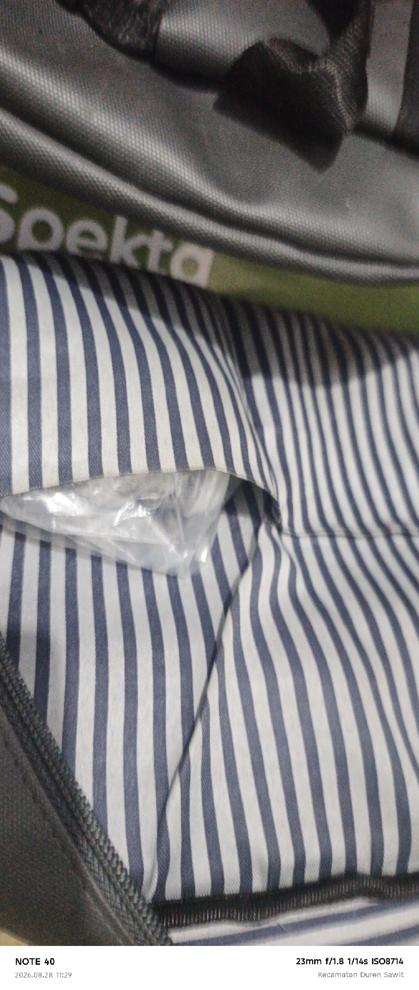 The image shows a close-up view of a striped fabric, possibly the interior lining of a bag. The stripes are alternating dark blue and white. In the upper left corner, a portion of a gray bag with the word "Spekta" visible is present. A clear plastic bag containing an unseen object is tucked into the folds of the striped fabric. The bottom of the image contains text indicating it was taken with a "NOTE 40" device on "2026.08.28 11:29" with camera settings "23mm f/1.8 1/14s ISO8714" and a location "Kecamatan Duren Sawit". This suggests the image was captured in the Duren Sawit subdistrict of East Jakarta, Indonesia.