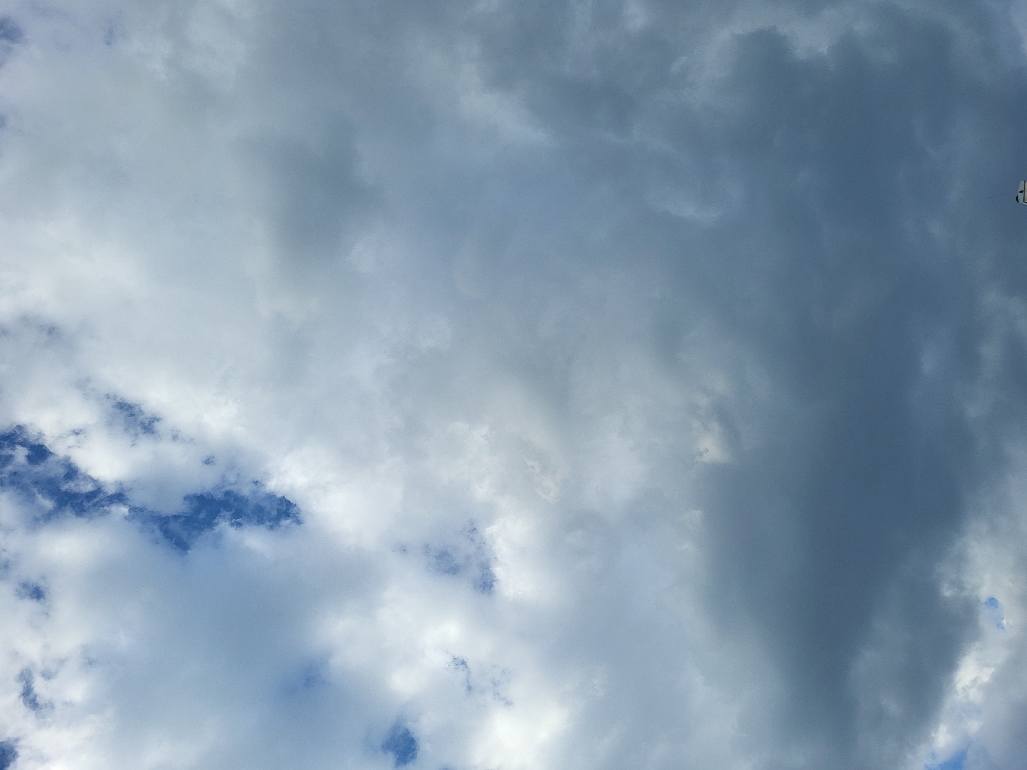 The image is a cloudy sky with patches of blue visible in the lower left corner. The clouds range in color from white to gray and dark gray. The location is unknown.