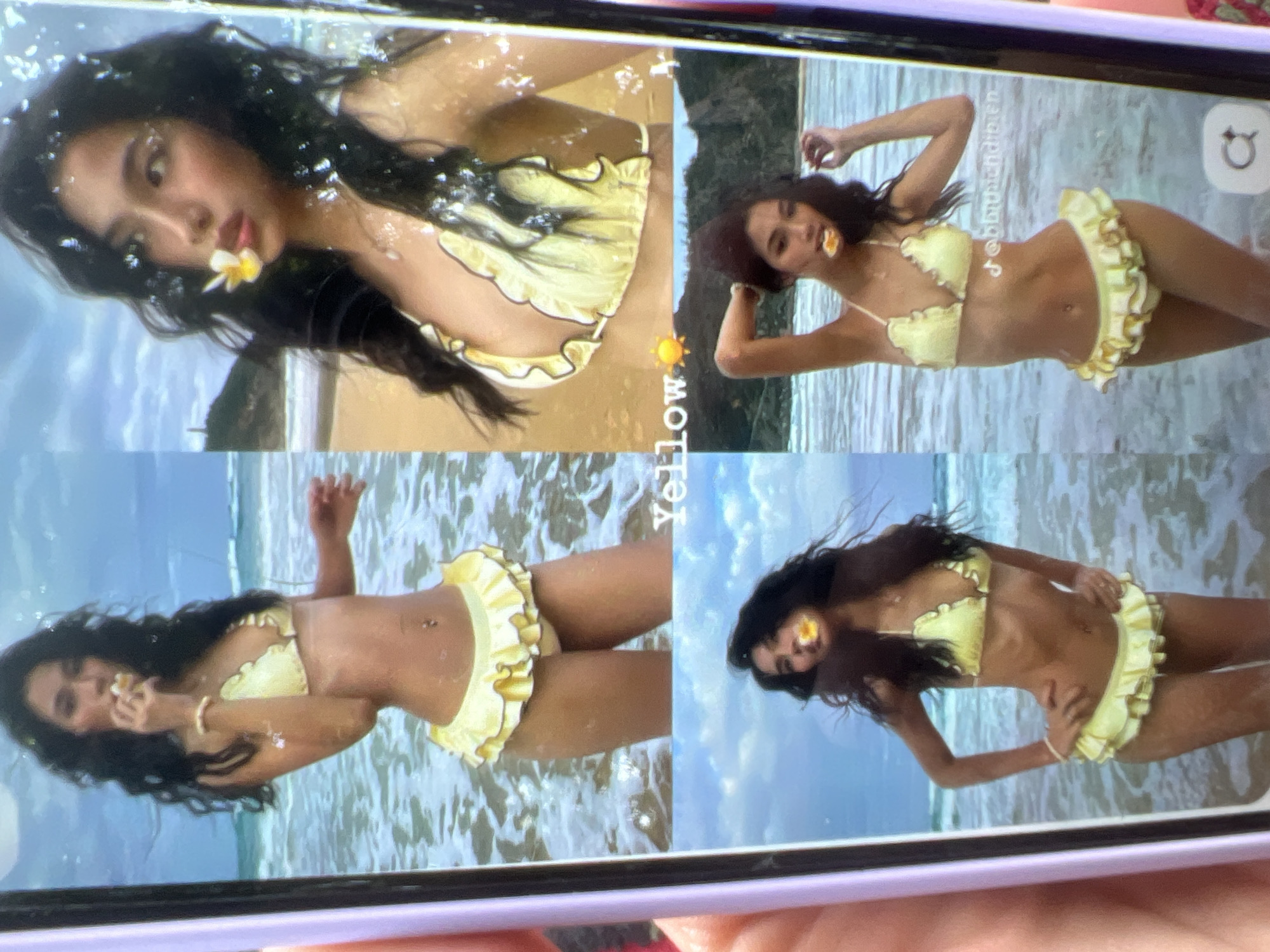 The image is a photograph of a person wearing a yellow bikini with ruffled edges, posing in the ocean. The person has dark hair and a flower in their mouth. The scene appears to be a beach or coastal area with waves and a sandy shore in the background. The image is presented on a phone screen, with reflections and light glare visible. The city of Kara-Dıykan, Kyrgyzstan is not depicted in this image.