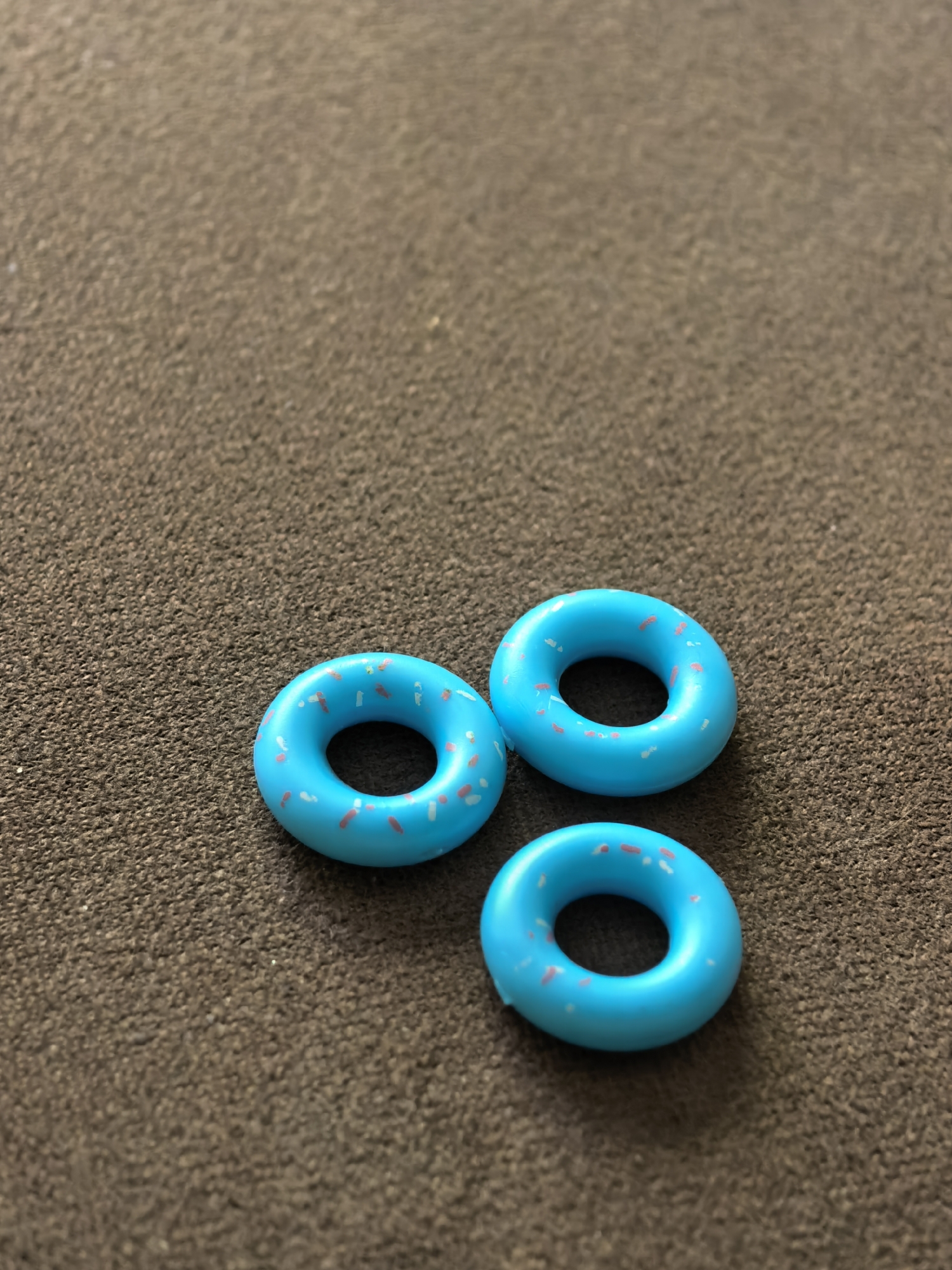 Three blue donut-shaped objects with pink sprinkles are arranged on a brown, textured surface. There is no indication of location in Sterlitamak, Russia or any people or actions.