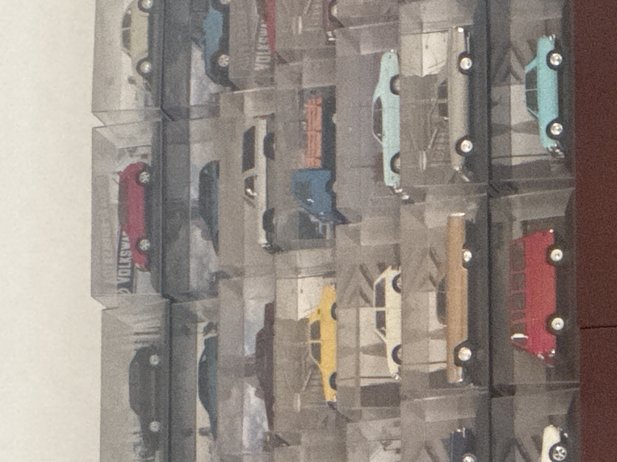 The image shows an array of die-cast Volkswagen Beetle toy cars, each enclosed in a transparent plastic case. The cars are arranged in a grid-like pattern on a white wall or background. The cases appear to be stacked or mounted on the wall. The colors of the cars vary, including red, blue, grey, yellow, and light blue. The backdrop appears to be an indoor setting.
I cannot know about the exact location in the city of Puebla, Mexico with this information.