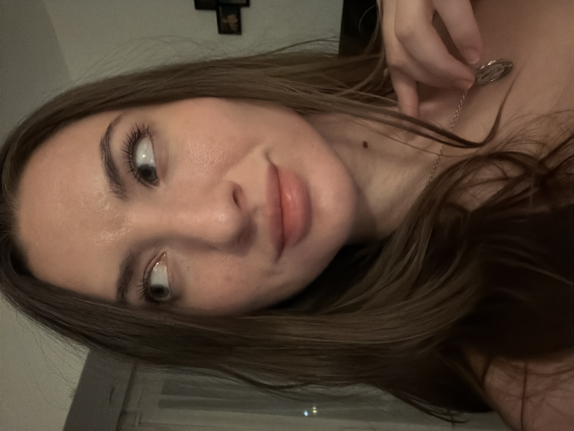 The image shows a close-up of a woman's face, with her head turned to the side and looking off-camera. She has long, brown hair, prominent eyelashes, and is wearing a necklace. The background is dimly lit, with hints of interior furnishings. The location in Sharm El Sheikh, Egypt is not depicted or suggested in the image.