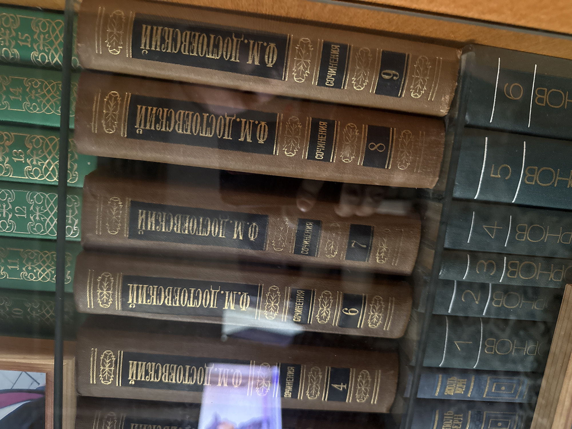 The image shows a bookshelf filled with books. The books are stacked horizontally and vertically, with their spines facing outward. The spines of many of the books display titles and author names in a foreign language, likely Russian, given the location context of Morozovka, Russia. Some books have dark green covers with gold lettering and ornate designs, while others have brown covers with similar gold embellishments. Visible text includes "Ф.М. ДОСТОЕВСКИЙ" and "СОЧИНЕНИЯ" on several spines, suggesting these are collected works of Fyodor Dostoevsky. Numbers such as "9", "8", "7", "6", "5", "4", "3", "2", "1", "12", "13", "14", and "15" are also visible, possibly indicating volume numbers. The lighting suggests an indoor setting, perhaps a library or a home with a well-stocked collection. The overall impression is one of order and intellectual pursuit, with the books arranged neatly on shelves. The image appears to have been taken at eye level, looking slightly upwards at the bookshelf. No people are visible in the frame. The scene is static, with no discernible activity.
--- OCR Start ---
EPH
BEPH
12
OPHOB
PHOB
4
6
7
8
PHOB
PHOBA
45
HOBO
OBの
Ф.М. ДОСТОЕВСКИЙ
Ф.М. ДОСТОЕВСКИЙ
СОЧИНЕНИЯ
СОЧИНЕНИЯ
СОЧИНЕНИЯ
СОЧИНЕНИЯ
СОЧИНЕНИЯ
6
12
13
Ф.М. ДОСТОЕВСКИЙ ||
Ф.М. ДОСТОЕВСКИЙ
--- OCR End ---