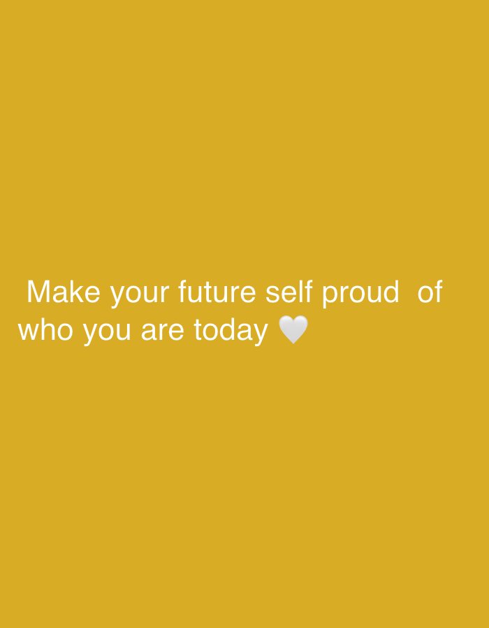 The image is a close-up shot of a light mustard-yellow background with the text "Make your future self proud of who you are today" written in white. A white heart emoji is located at the end of the text. There are no people, objects, or other environmental details in the image. The location is not discernible from the image content.