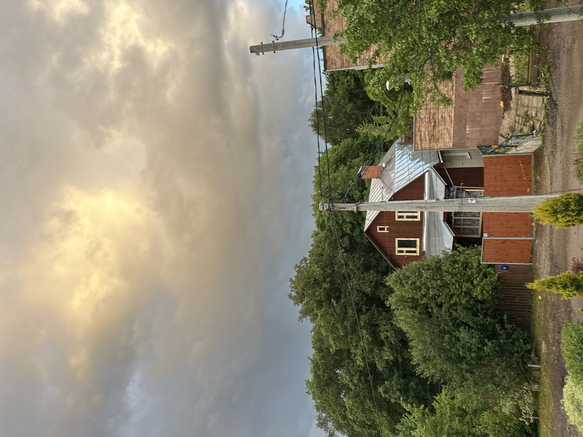 The image shows a house on a street in Nizhny Novgorod, Russia. The house is surrounded by trees. A street and an overcast sky are visible. Overhead power lines extend over the house and street. A fence and gate are adjacent to the house.