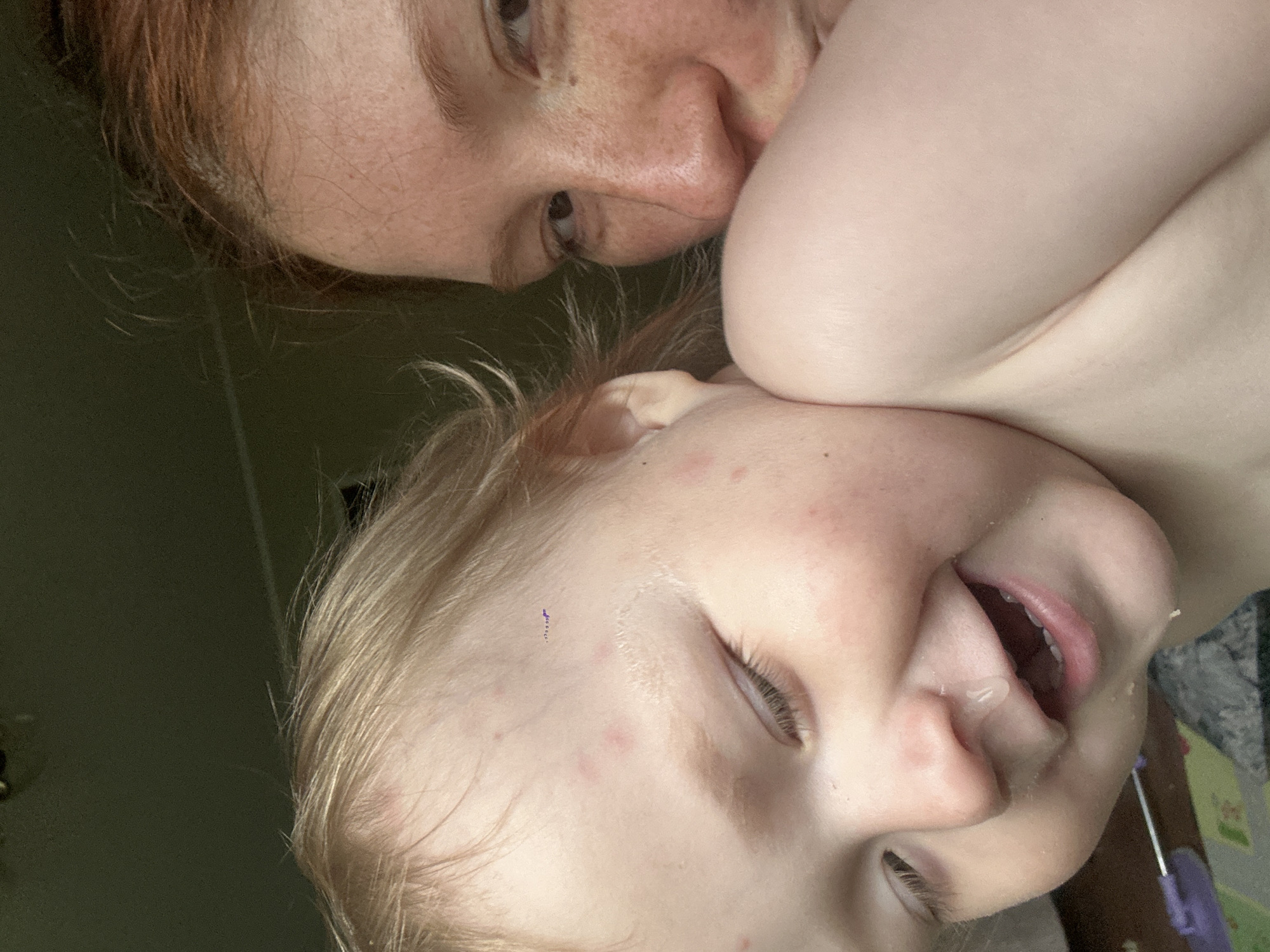 A close-up shot shows a person with red hair and freckles with their face close to the face of a young child with blonde hair. The child's eyes are mostly closed, and their mouth is open, with some liquid visible near their nose. The background is blurry and dark. There is no indication of the location being in Nizhny Novgorod, Russia.