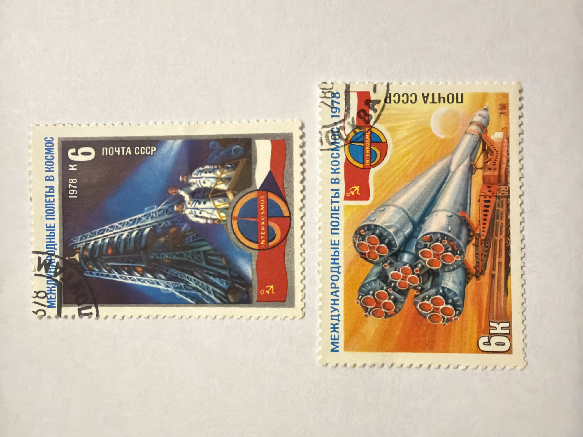 The image contains two Soviet Union postage stamps from 1978, commemorating the "International Flights in Space" program. Both are rectangular with serrated edges. The stamp on the left depicts a space station or orbital complex with cosmonauts visible, set against a backdrop of blue and the Interkosmos program logo, which includes a flag representing participant nations and the Soviet hammer and sickle emblem. The denomination is "6 K" (Kopeks). The stamp on the right shows a launch vehicle, presumably a Soyuz rocket, on its launchpad against an orange-yellow sky with the sun and the moon. The same Interkosmos logo appears, along with another "6 K" denomination, and the text "ПОЧТА СССР" (Post of the USSR). A handwritten "5/8" appears on the stamp with the space station. There is no evidence to indicate that this image was taken in Izhevsk.
