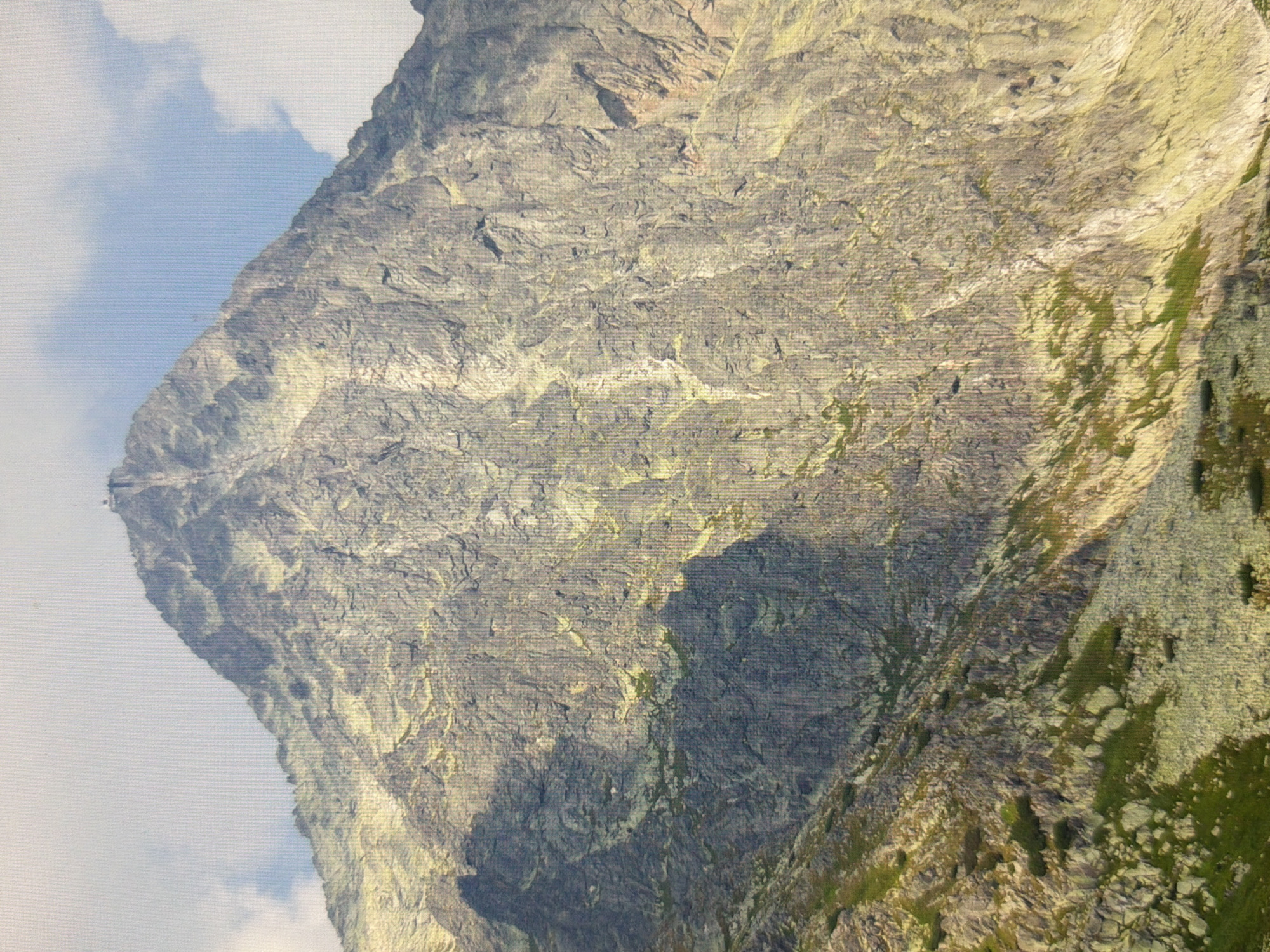 The image displays a rocky mountain peak under a cloudy sky. A small structure is visible at the summit. The mountain slopes are covered with scree and patches of vegetation. The scene is a natural landscape, not a cityscape, and therefore cannot be located in Kyiv, Ukraine.