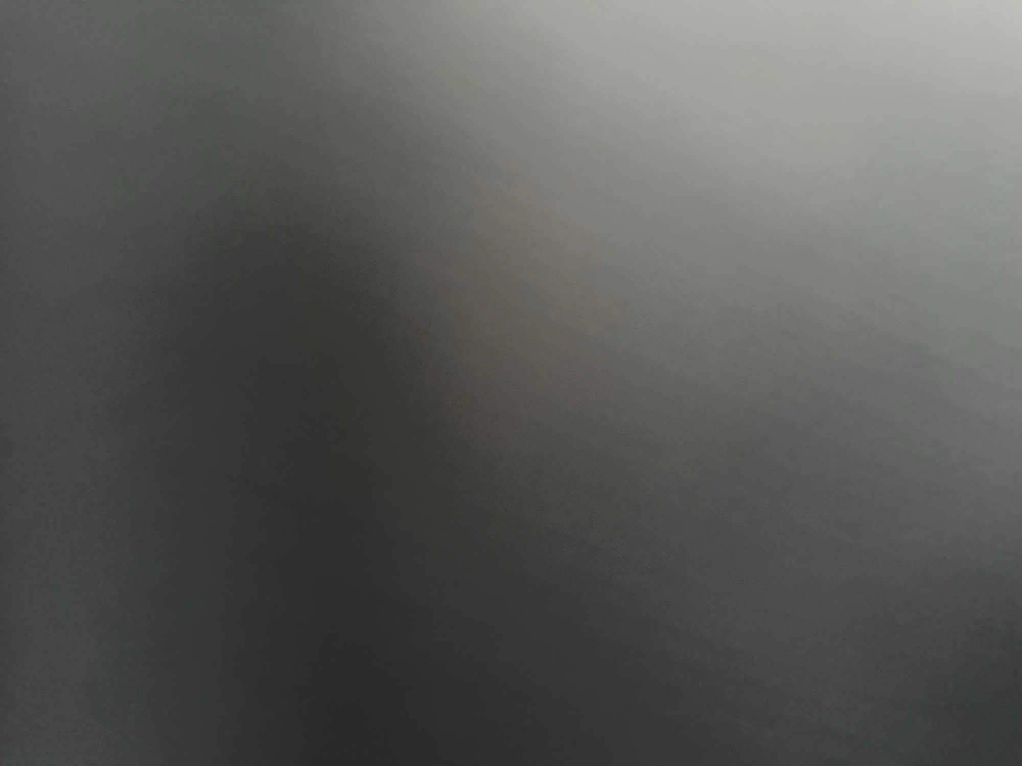 This is an abstract, monochromatic photograph with a gradient of gray tones. The left side of the image is significantly darker, fading into lighter shades of gray towards the right. There are no discernible subjects such as people, objects, or a clear scene. The lighting appears to be diffuse, with the brighter area suggesting a light source from the upper right, though its nature is not identifiable. The texture is subtle, with a slight grain visible upon closer inspection, indicative of a textured surface or image noise. There are no visible cues for time of day, weather, location, or emotions. No text is present in the image. The context of Belgrade, Serbia, does not provide any specific visual information for this abstract photograph.