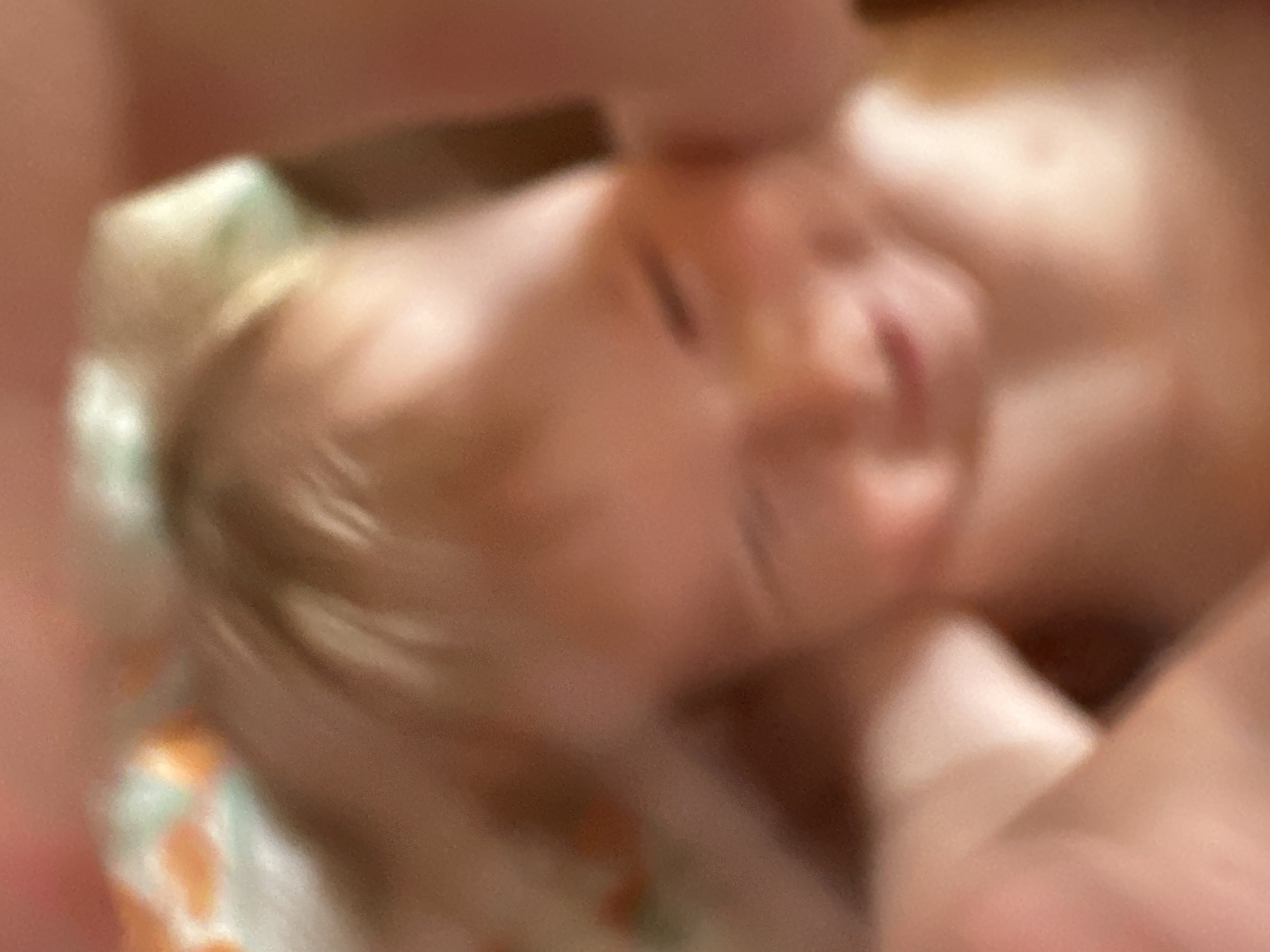 The image appears to show a blurred close-up of a baby, possibly lying on a patterned cloth. The baby has light hair. The location is not discernible from the image.