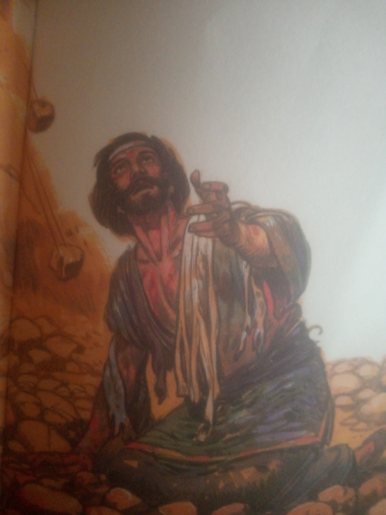 The image shows a painting of a man in a distressed state, with his head tilted upwards and his arm outstretched. He has a beard and is wearing a headband, a draped cloth around his shoulders, and a garment around his waist. The background appears to be a rocky or barren landscape. There is no discernible depiction of Jauro Yinu, Nigeria, or any other specific location in the city. The painting is focused on the solitary figure and does not provide any contextual clues about its setting within a city or any Nigerian context.