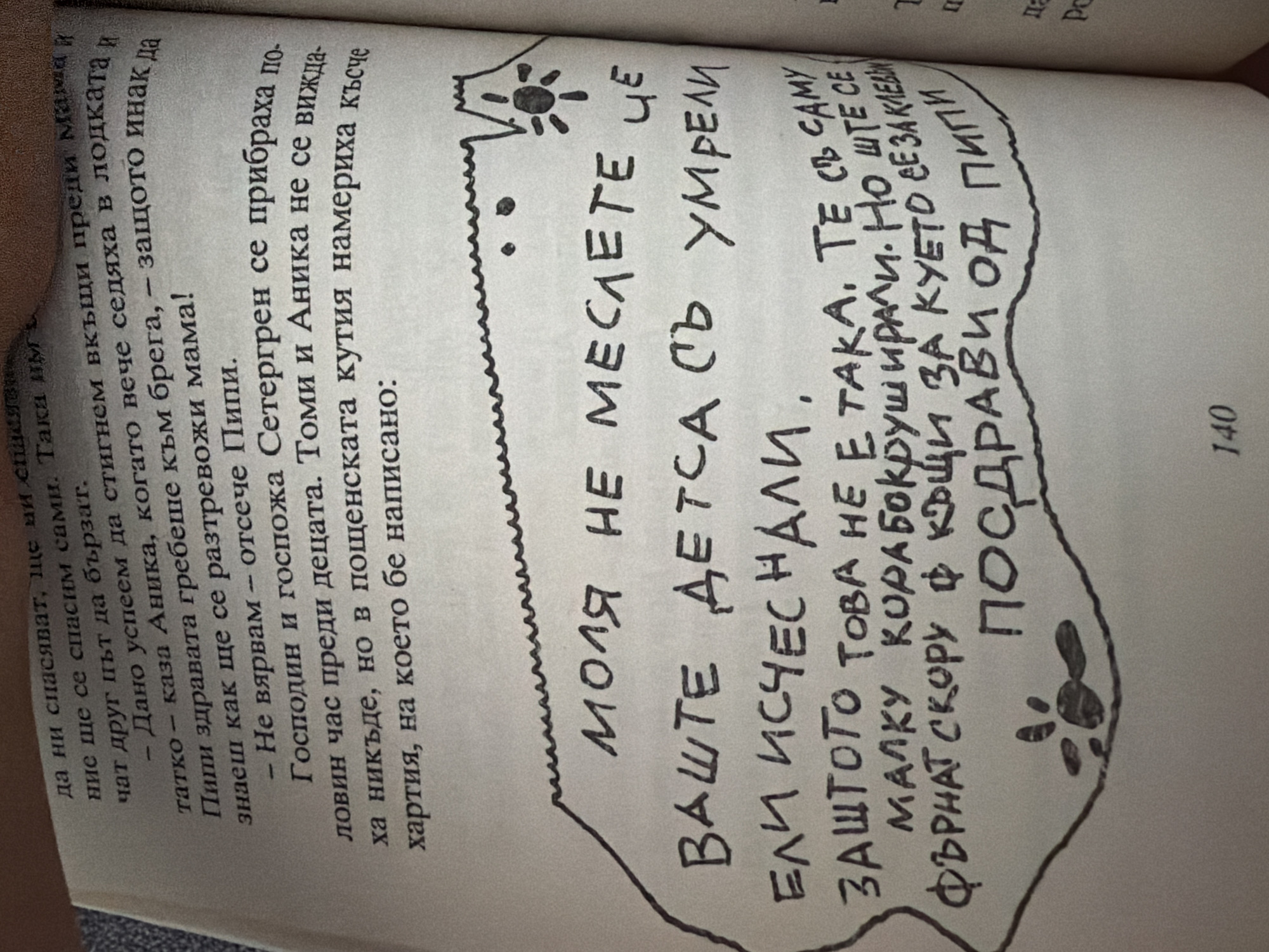 The image shows a page from a book with handwritten text and a drawing. The printed text at the top describes a story. The handwritten text, enclosed within a jagged border, contains a message in Bulgarian. The drawing includes a depiction of a mountain range with a sun and a paw print. The page number "140" is visible at the bottom. There is no information in the image that relates to the city of Pazardzhik, Bulgaria, or any specific location. The handwritten text reads: "Моля не меслете, че вашите деца съ умрели, ели исчезнали, защото това не малку корабокрушили. Но ще се фърнат скору ф куето е за клавии, поздрави од пипи." This translates to: "Please do not think that your children have died or disappeared, because not many shipwrecks. But they will be thrown soon into the kennel, greetings from Pippi."