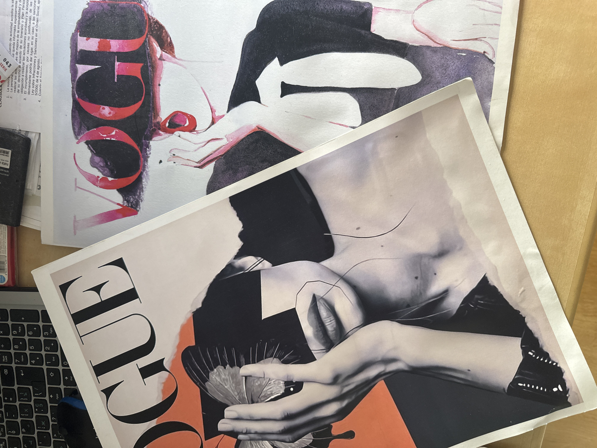 The image displays two Vogue magazine covers, one layered partially over the other, set against a wooden surface. The left magazine features a bold "VOGUE" logo in black, accompanied by a striking graphic of a woman's face fragmented with geometric shapes and a butterfly resting on her hand. The right magazine also prominently features the "VOGUE" logo in red and pink, superimposed over an illustration of a woman's head wearing a wide-brimmed hat, her mouth open and her hand near her face. A small portion of text, possibly from another document, is visible at the top of the image, with some characters suggesting it may be in Spanish and referencing "Murcia, Spain." The lighting suggests an indoor environment, likely a desk or table surface.