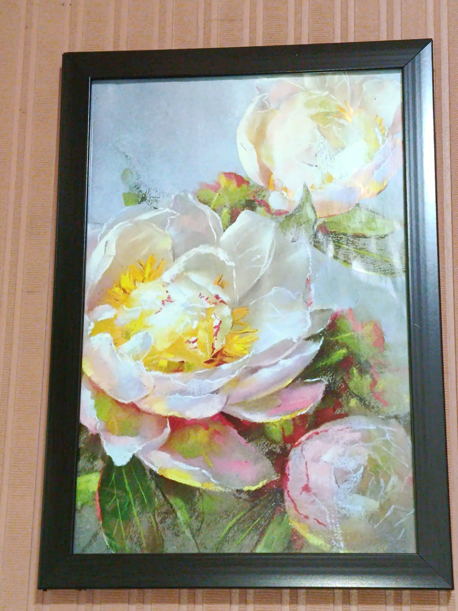 This is a framed painting of peonies hanging on a wall. The painting features several white and pink peonies with yellow centers, against a muted blue background. The frame is dark and rectangular. The wall behind the painting has a textured, vertical striped pattern in a light peachy-pink color. The scene is indoors, with no indication of a specific location in Tashkent, Uzbekistan.