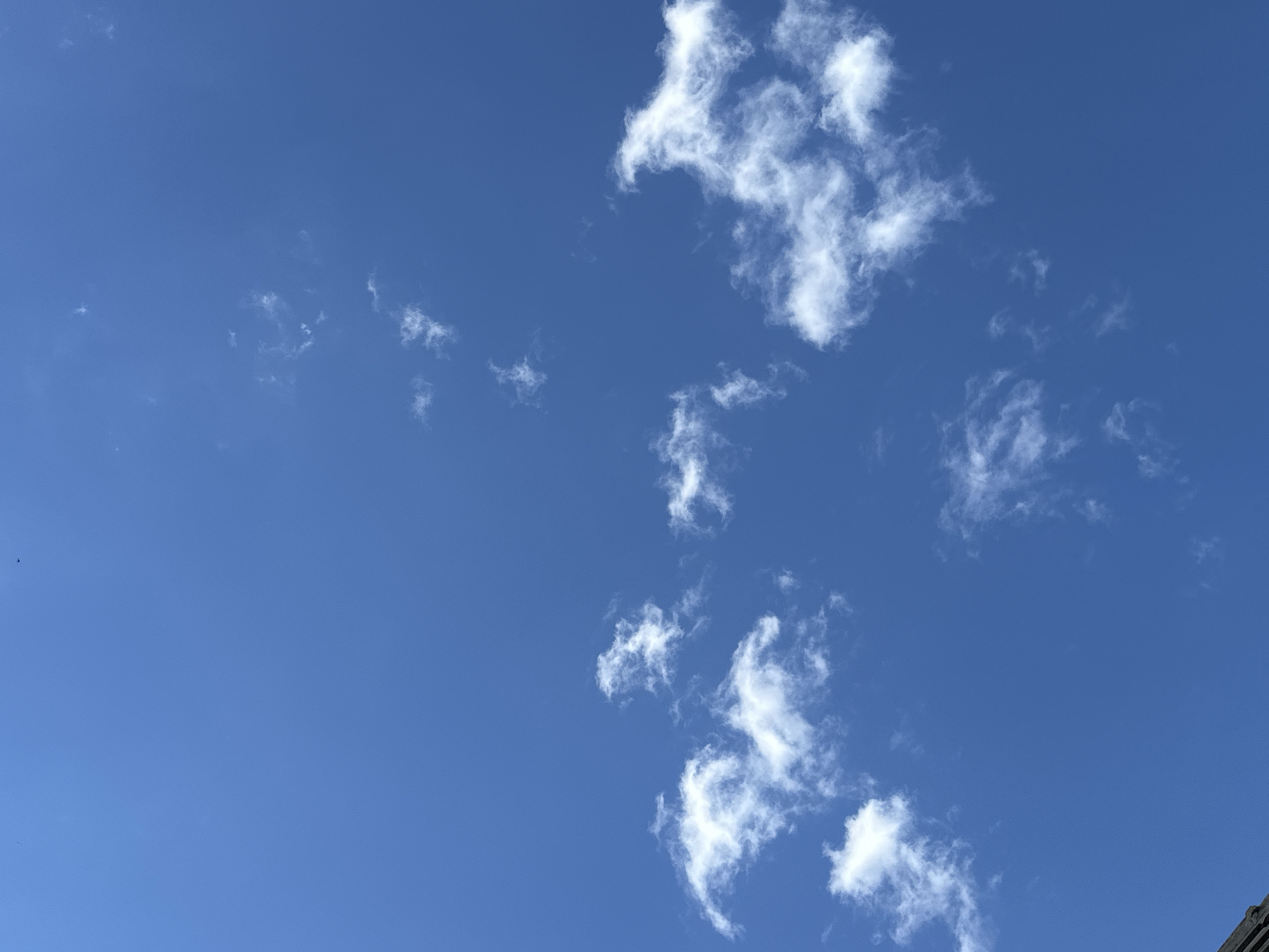 A clear blue sky with scattered white clouds. In the lower left corner, a portion of a building with a dark, textured roof is visible. There are no people or animals in the frame. The scene appears to be an outdoor view, possibly from a rooftop or a higher vantage point. The image does not contain any specific landmarks or indicators that would allow for the precise identification of its location within Luhansk, Ukraine.