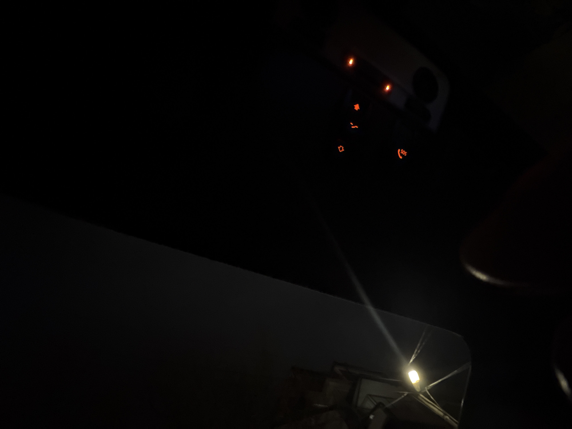 The image, taken at night, appears to be from inside a car. The dashboard indicator lights are illuminated. Reflected in what is likely the side mirror, a street lamp is visible outside the vehicle. There are no people visible. The location is unknown, but based on the request, it could be Varna, Bulgaria. More information is needed to determine where it is in Varna, Bulgaria.