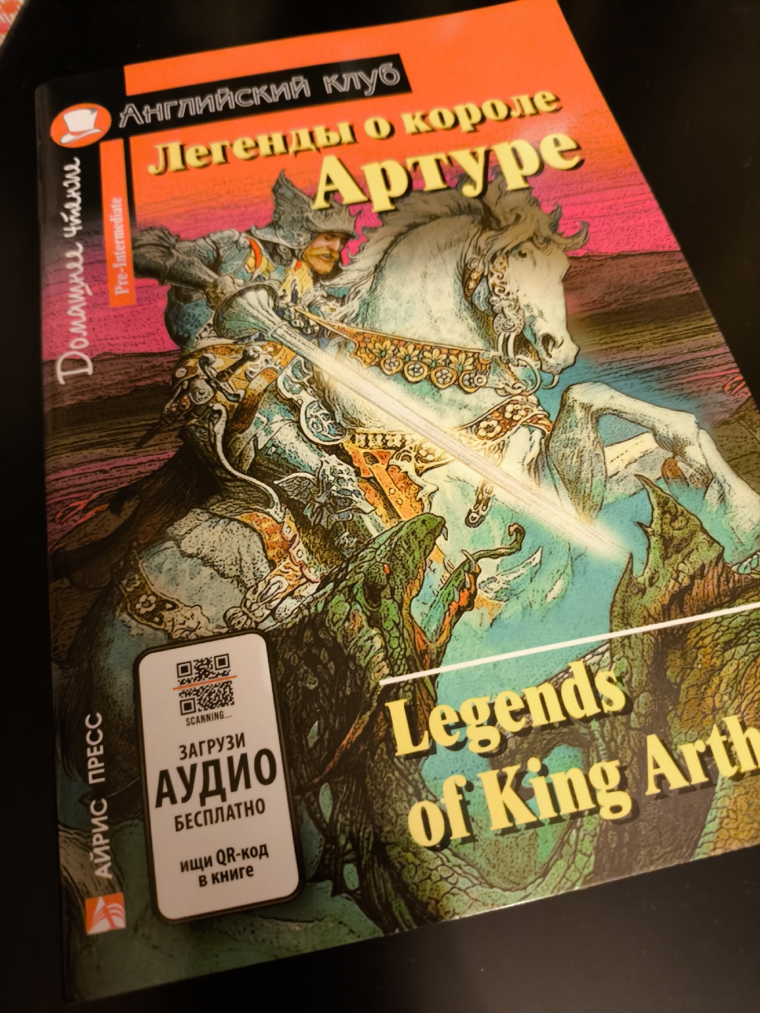 The image shows a book cover titled "Legends of King Arthur" in both English and Russian ("Легенды о короле Артуре"). The book is part of the "English Club" series and is labeled as "Pre-Intermediate." The cover features an illustration of a knight on a horse. A QR code is prominently displayed on the cover, inviting the reader to download the audio version of the book for free. The book is published by "Айрис пресс." There is no indication of location in Khimki, Russia.