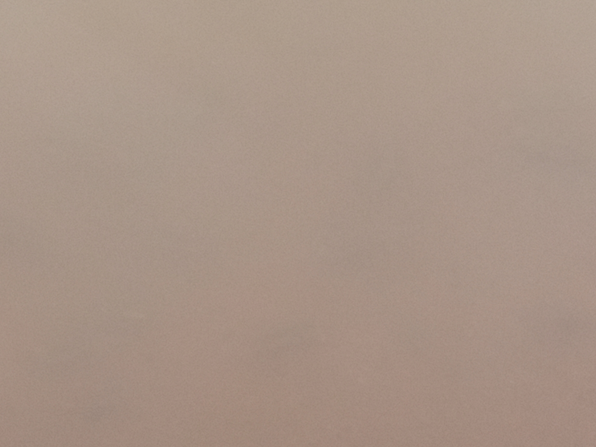 This is a photograph of a textured surface, likely fabric or paper, in a neutral, light brown or taupe color. The texture appears to be fine and slightly grainy, with subtle variations in shading that suggest an uneven surface at a microscopic level. There are no discernible objects, people, or environmental features present in the image. The photograph is a flat, evenly lit shot with no shadows. The location in Nanka, Nigeria, is not visible in this image.
