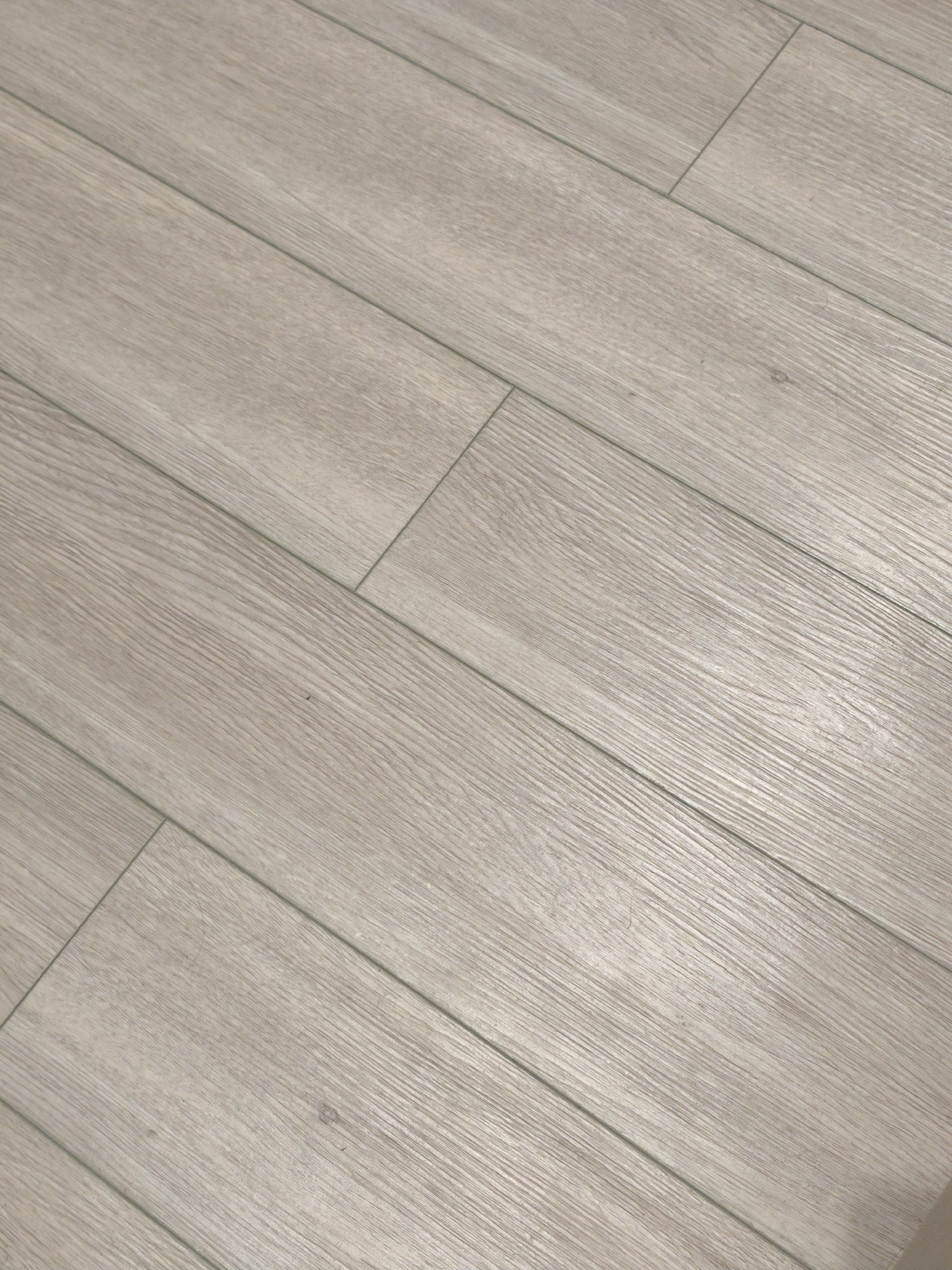 The image shows a close-up view of light-colored, wood-grain patterned floor tiles, likely indoors. The tiles are laid out in a parallel pattern, with thin grout lines separating them. The lighting is diffused, creating a soft, even illumination across the floor. There is no information to determine the location is Moscow, Russia.
