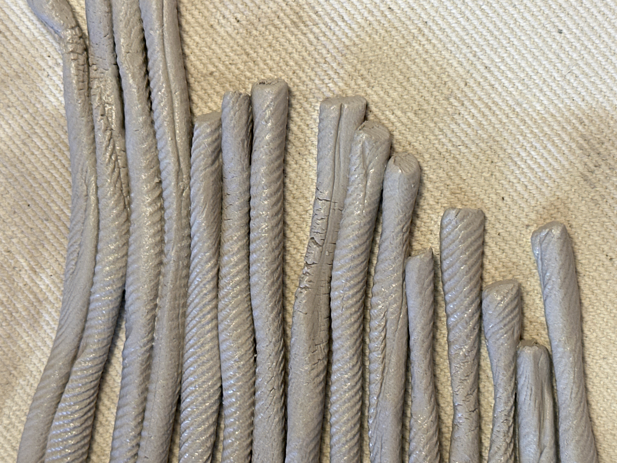 The image displays several gray, rope-like objects laid out horizontally on a textured, light-colored surface, possibly fabric. The objects are arranged in rows, with some overlapping. Each object appears to be a twisted cord, exhibiting a ridged texture. The lighting suggests an indoor setting. There are no people or any indications of the city of Nevinnomyssk, Russia within the image.