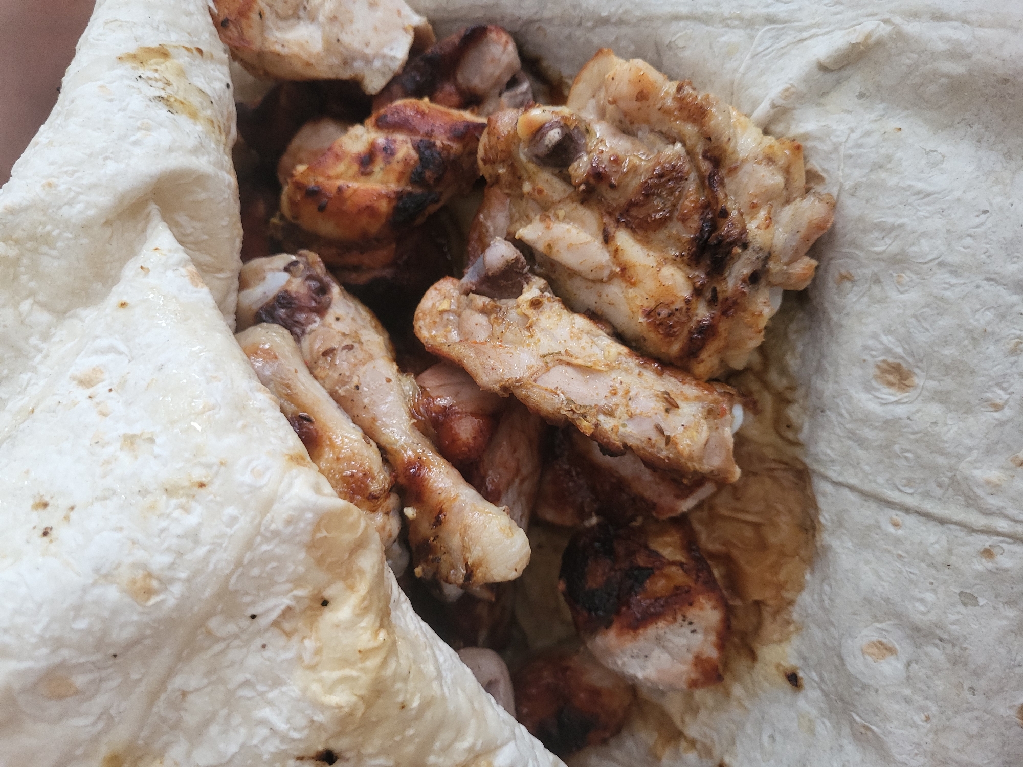 The image shows pieces of grilled chicken, some with bones, served in a folded flatbread. The chicken pieces are browned and appear to be cooked through. The flatbread is light in color with a slightly rough texture. The location, Зипуново, Russia, cannot be confirmed from this image alone.
