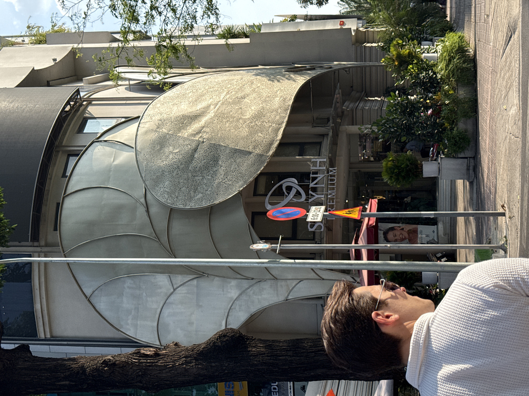 A man wearing sunglasses and a white textured top is observed near the building. The environment contains signage including a traffic sign and the building's name "SS LYNH PREMIUM". The location is identified as being in the city of Thủ Đức, Vietnam.