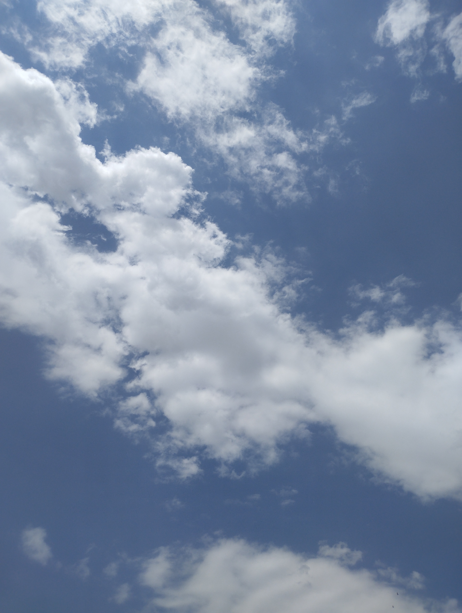 The image displays a clear, deep blue sky with scattered white cumulus clouds. The clouds are a mix of fluffy formations and wispy streaks, suggesting a partly cloudy day. There are no visible landforms, buildings, or people. The scene is entirely focused on the atmospheric conditions. The photograph appears to have been taken from an upward-looking perspective.