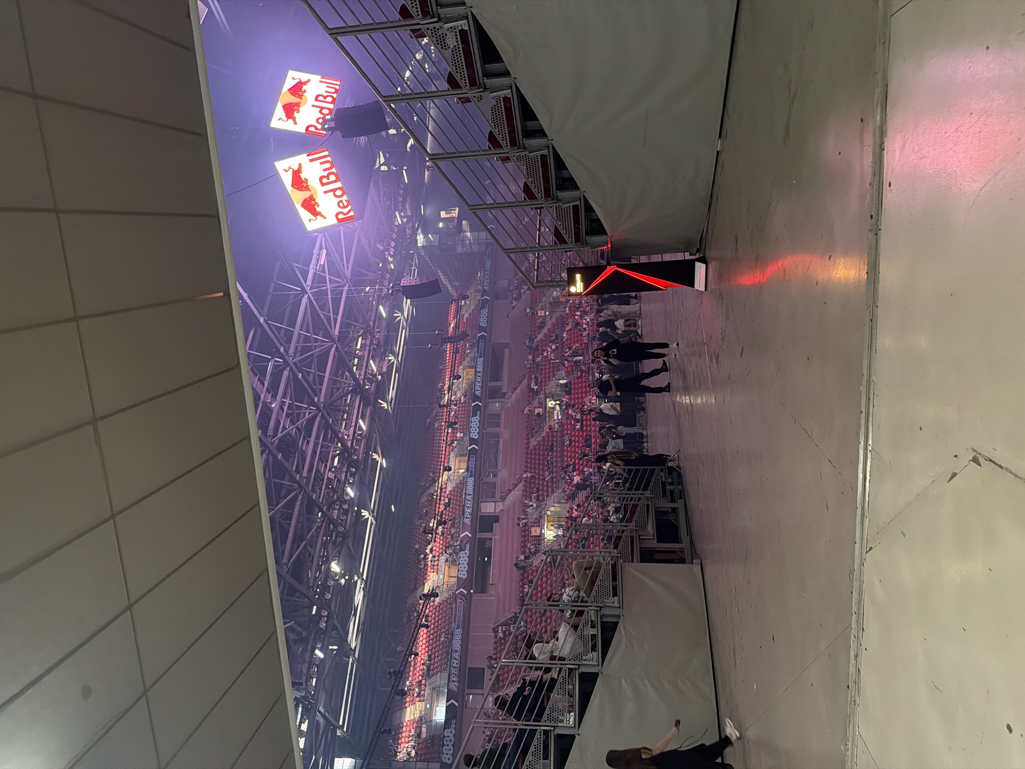 The image depicts the interior of Arena Sofia in Sofia, Bulgaria, filled with spectators. Two large Red Bull logos are prominently displayed. People are walking and gathering near the seating areas. The arena is well-lit, with scaffolding and metal structures visible above the seating. Text reading "APEHA 8888" and "APENA 8888 София 8888" is visible on the stadium's sidewalls.