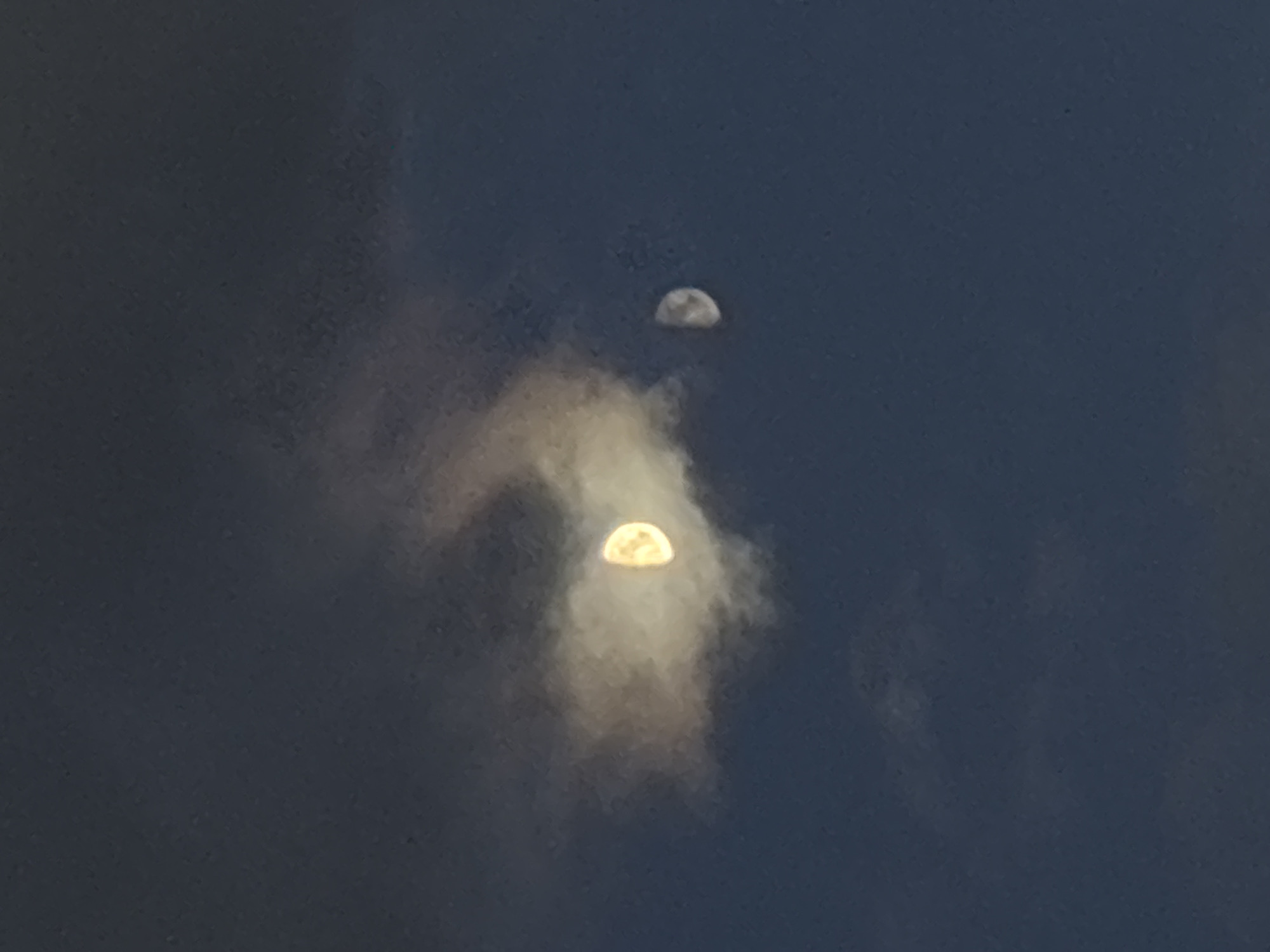 The image depicts two partially visible crescent moons in a dark blue sky, obscured by clouds. The lower moon is brighter and more prominent, with a golden glow. The upper moon is fainter. The location of the image is Saint Petersburg, Russia.