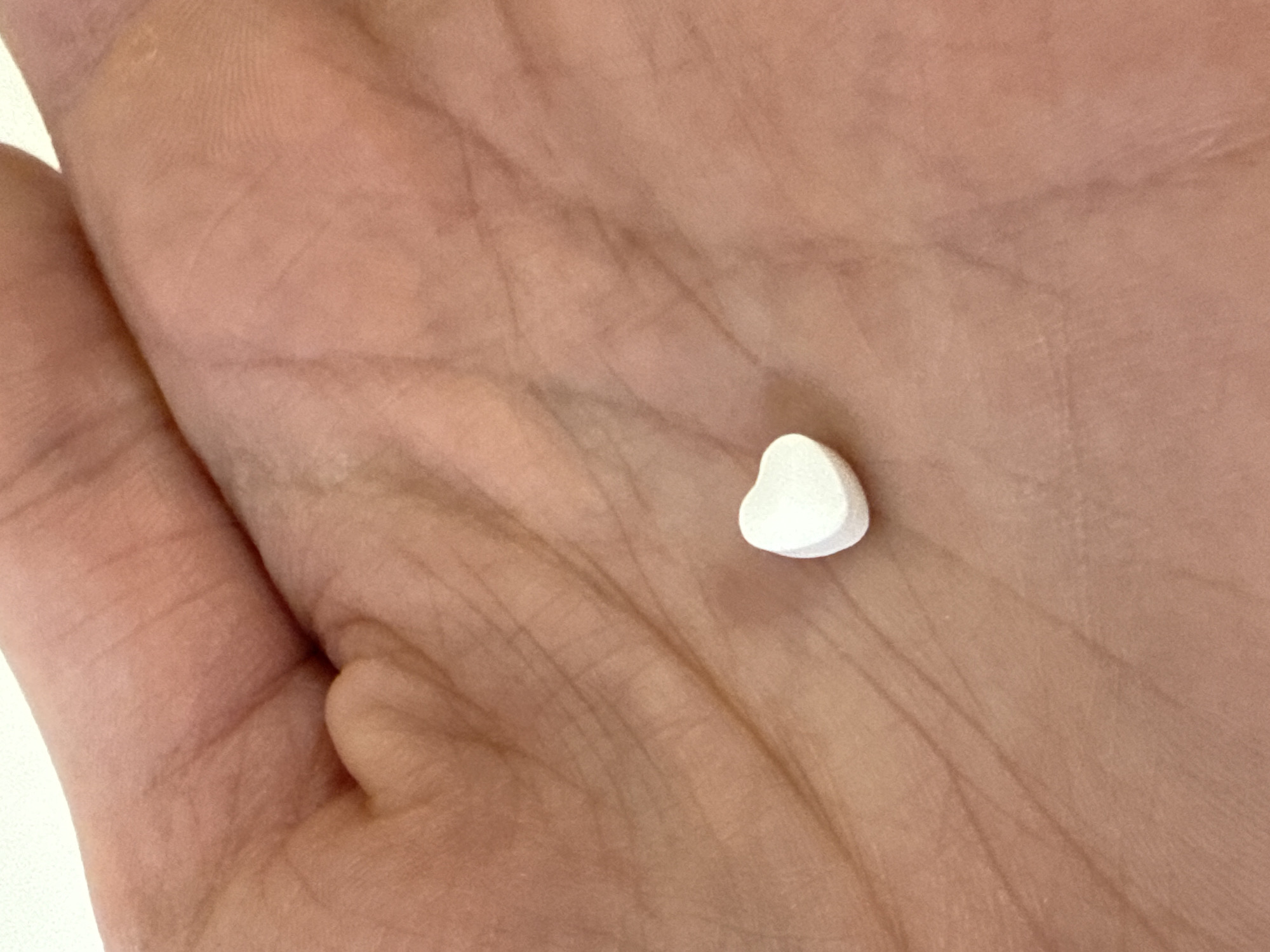 A close-up shot displays a white, heart-shaped tablet resting in the palm of a human hand. The skin tone of the hand is light. The background is out of focus. The location is not discernible from the visual information provided, therefore I cannot specify the location within the city of Pleven, Bulgaria.