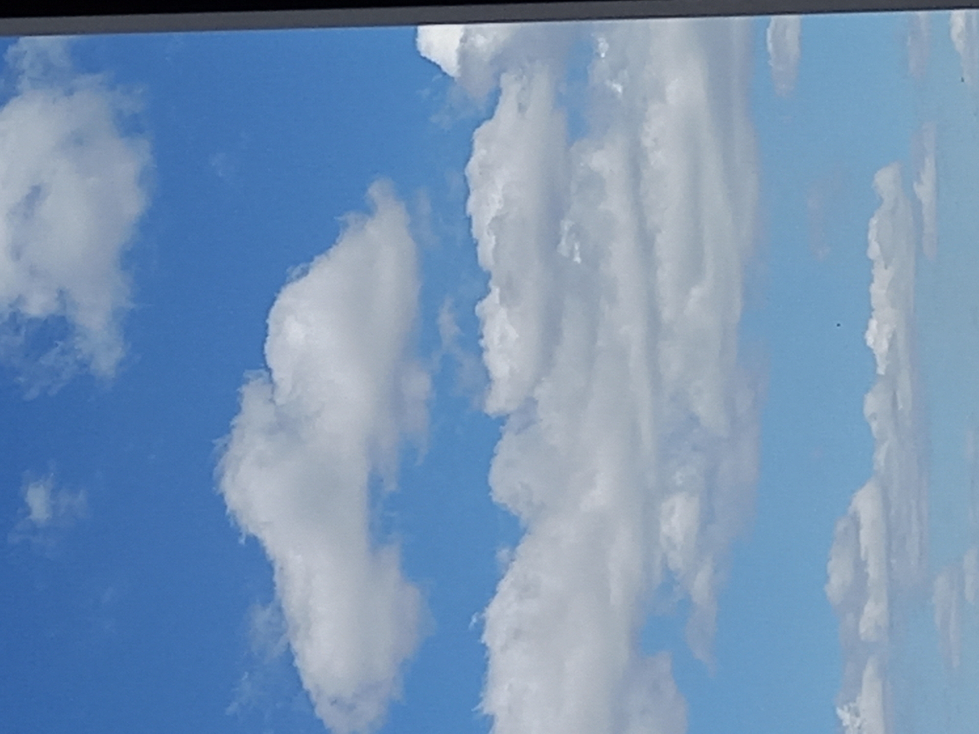 The image shows a blue sky with white clouds. The clouds are scattered across the sky, with some being more dense and elongated than others. There is no indication of the location being a city.